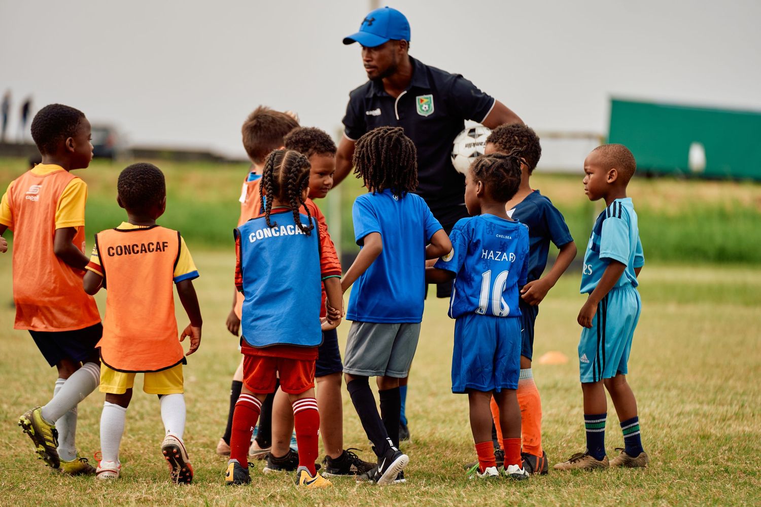 Young soccer players in colorful jerseys stand in a line on a grassy field during practice or a game.