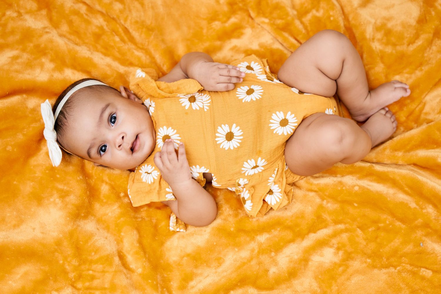 Baby lies on plush orange velvet blanket wearing floral outfit.