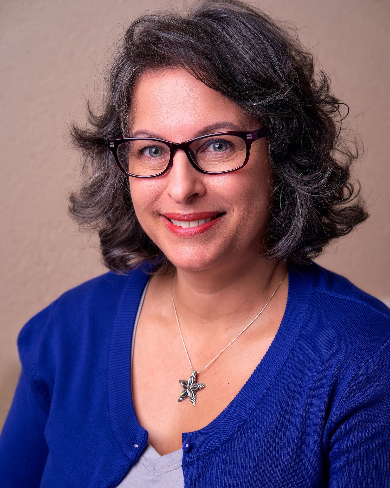 Professional headshots of someone in a blue blazer and glasses against a neutral background.