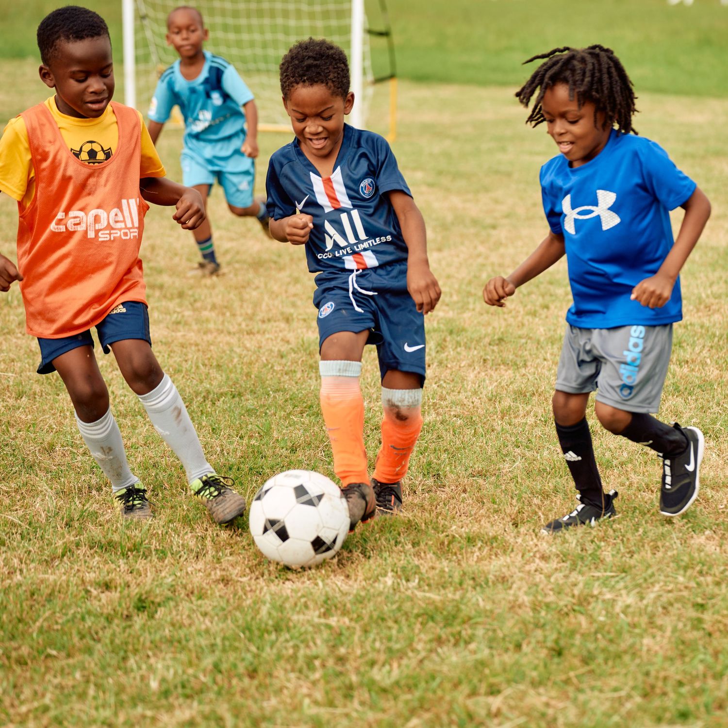 Young soccer players in colorful jerseys practice dribbling skills on a grassy field during a training session.