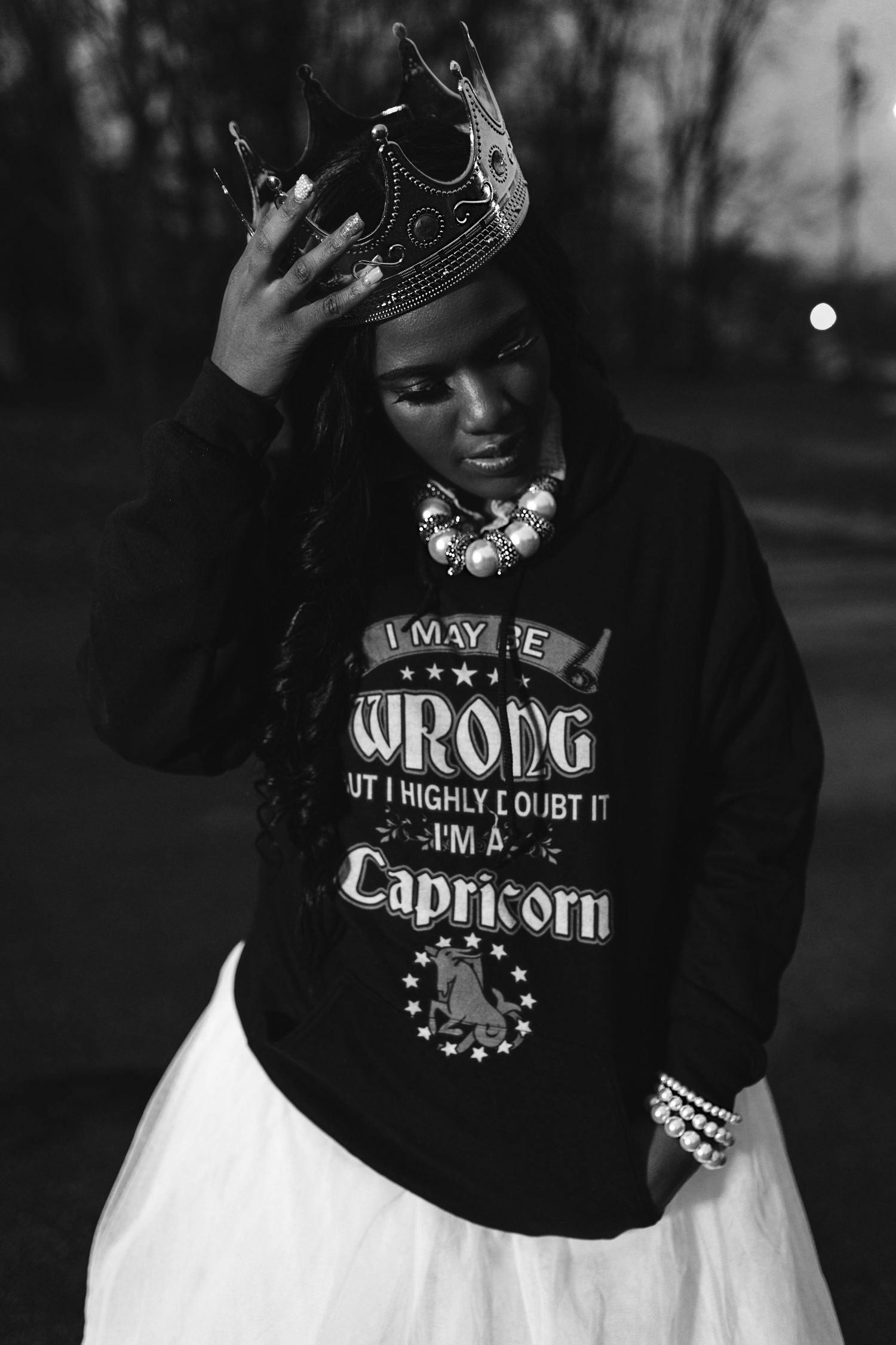 A black and white photo series showing someone wearing a hooded sweatshirt with Capricorn zodiac text and jewelry.