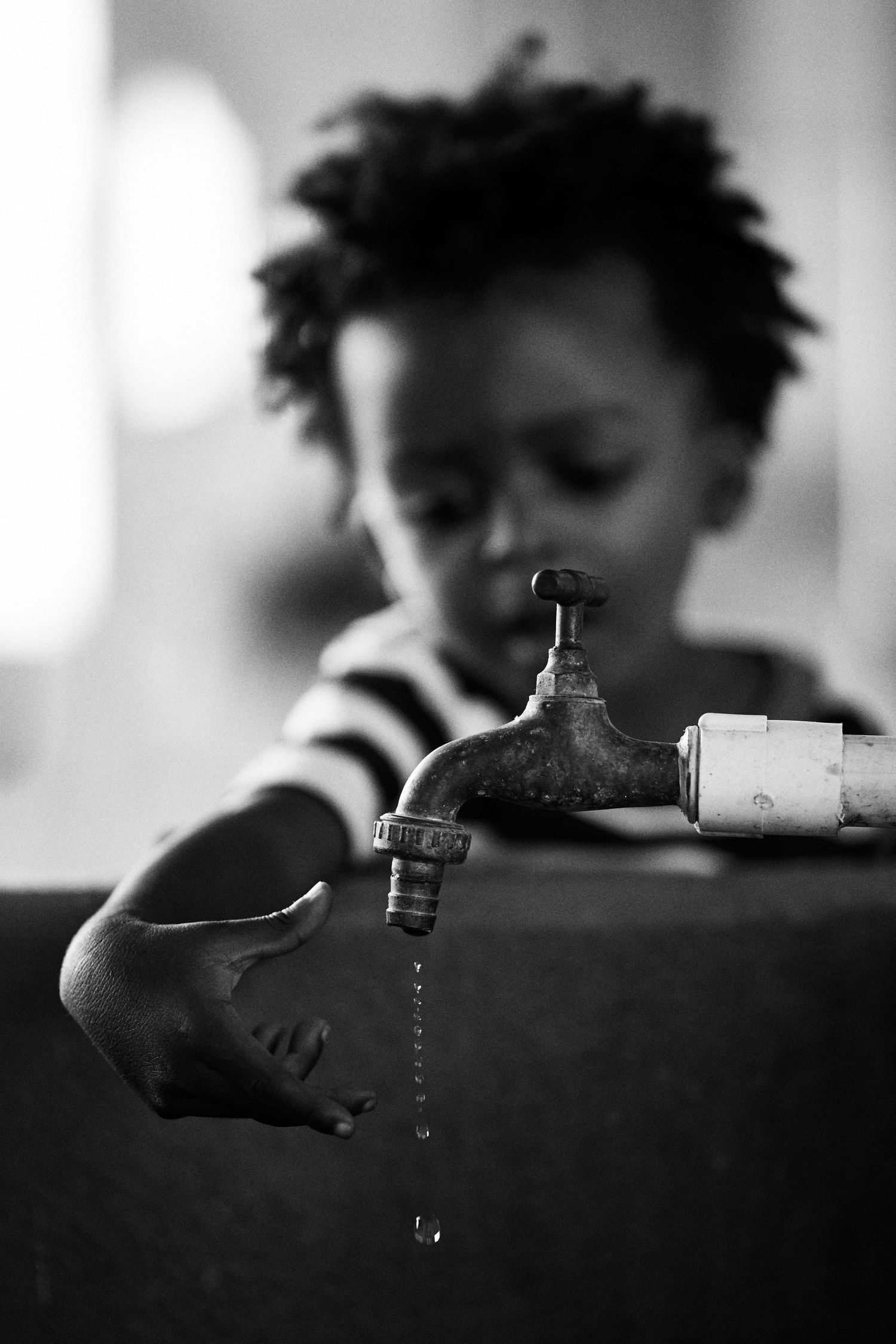 A black and white photograph shows a water faucet dripping with a blurred background.