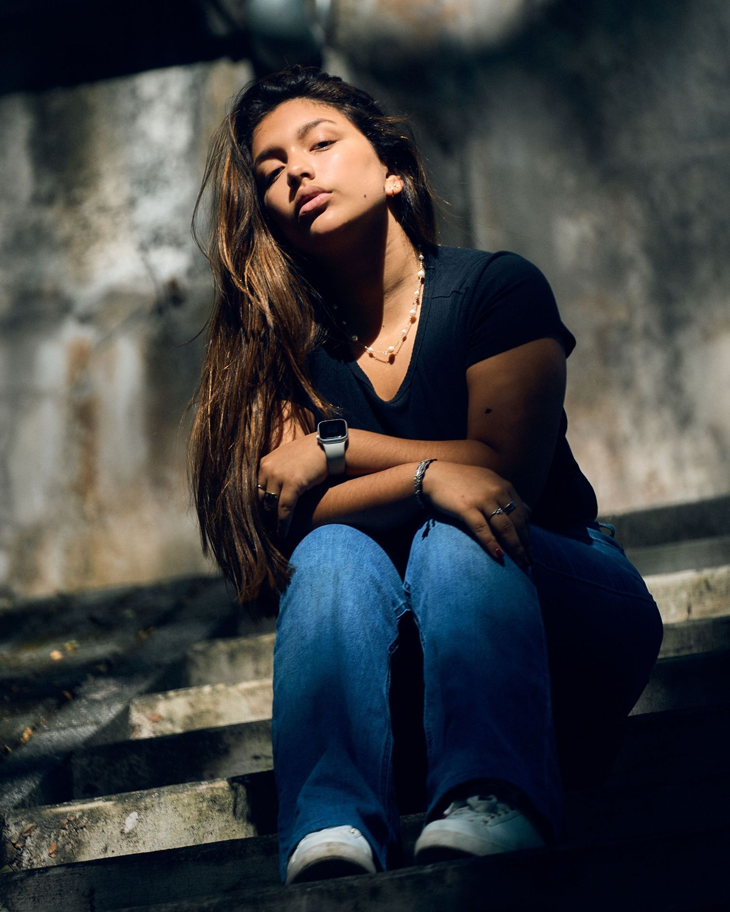 A moody portrait of someone in casual attire sitting on concrete steps in dramatic lighting.