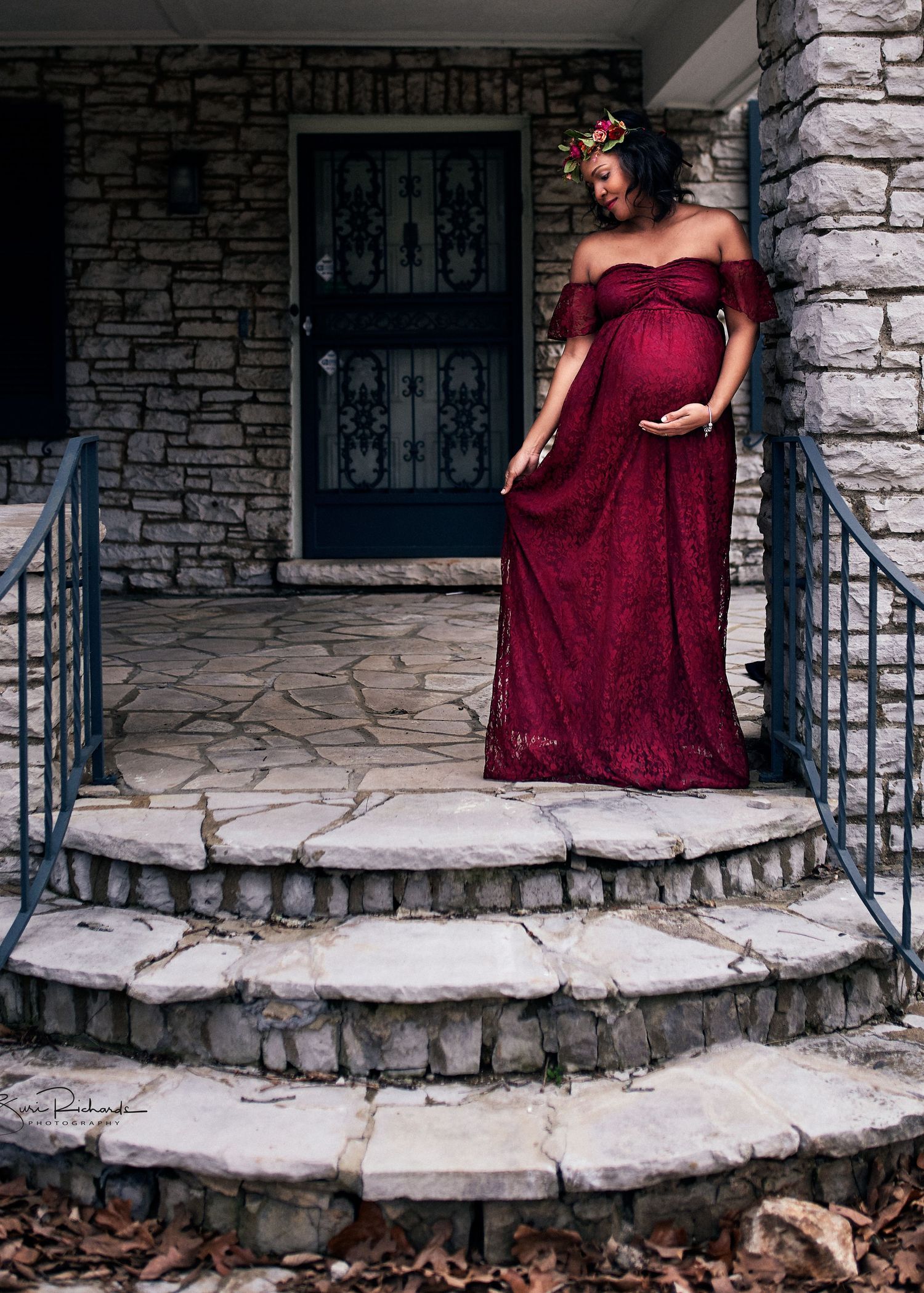 Person in burgundy formal dress posing on stone steps with architectural details.
