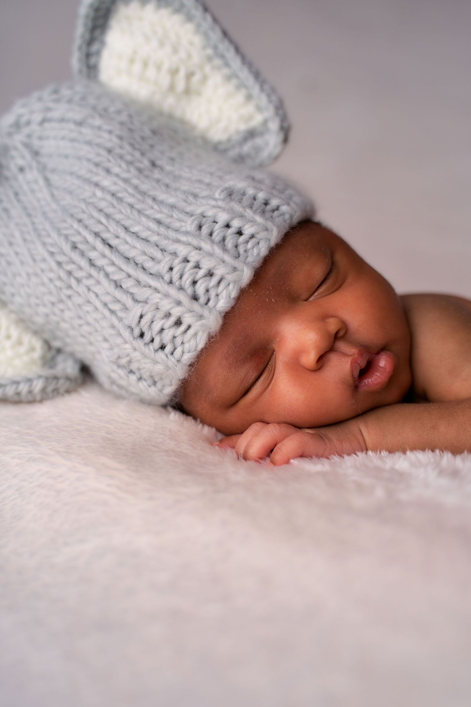 A sleeping newborn baby wearing a soft gray knitted hat rests peacefully on white bedding.