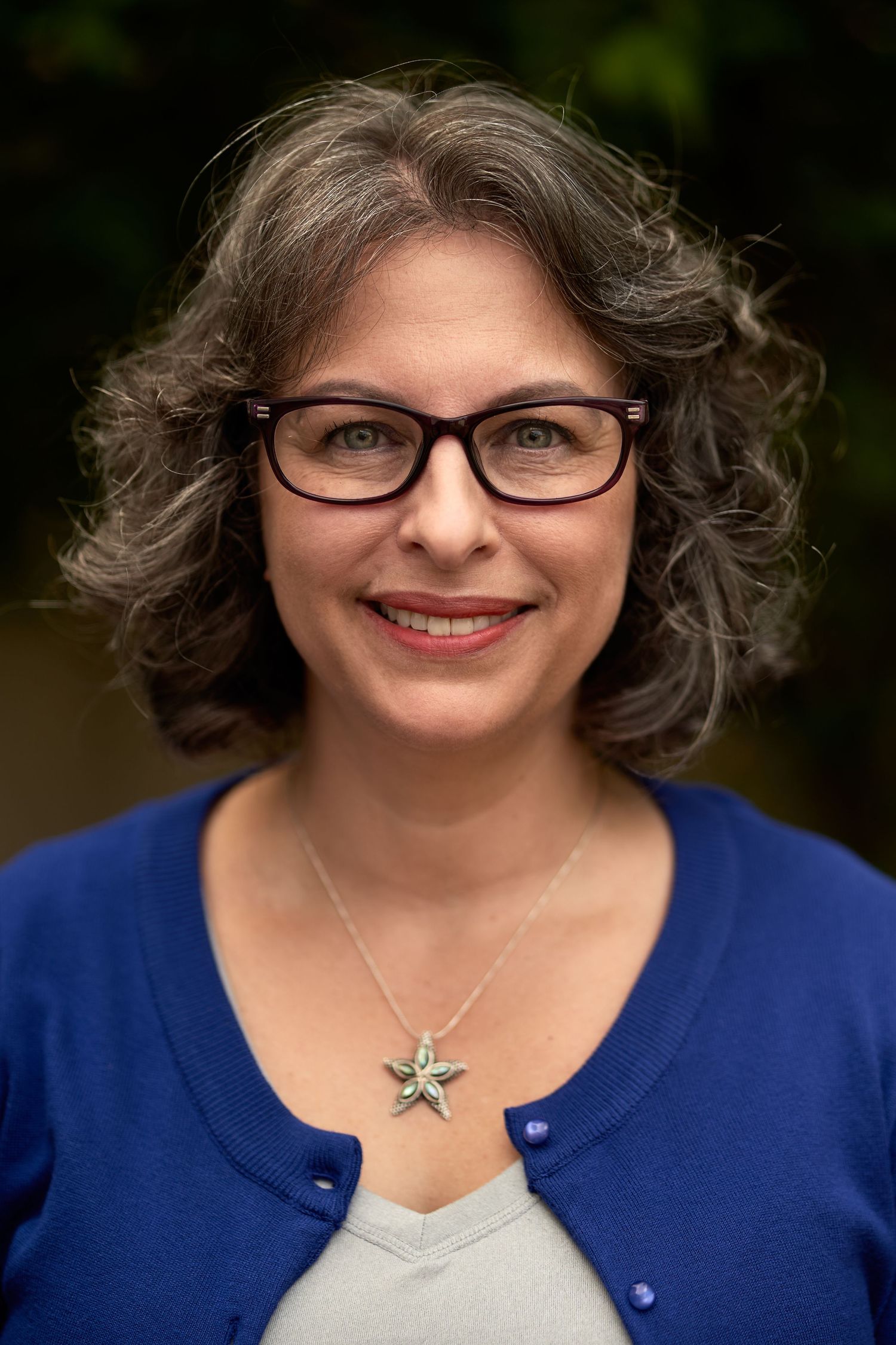 Portrait series showing a person with curly hair wearing glasses and a blue cardigan with a star necklace.