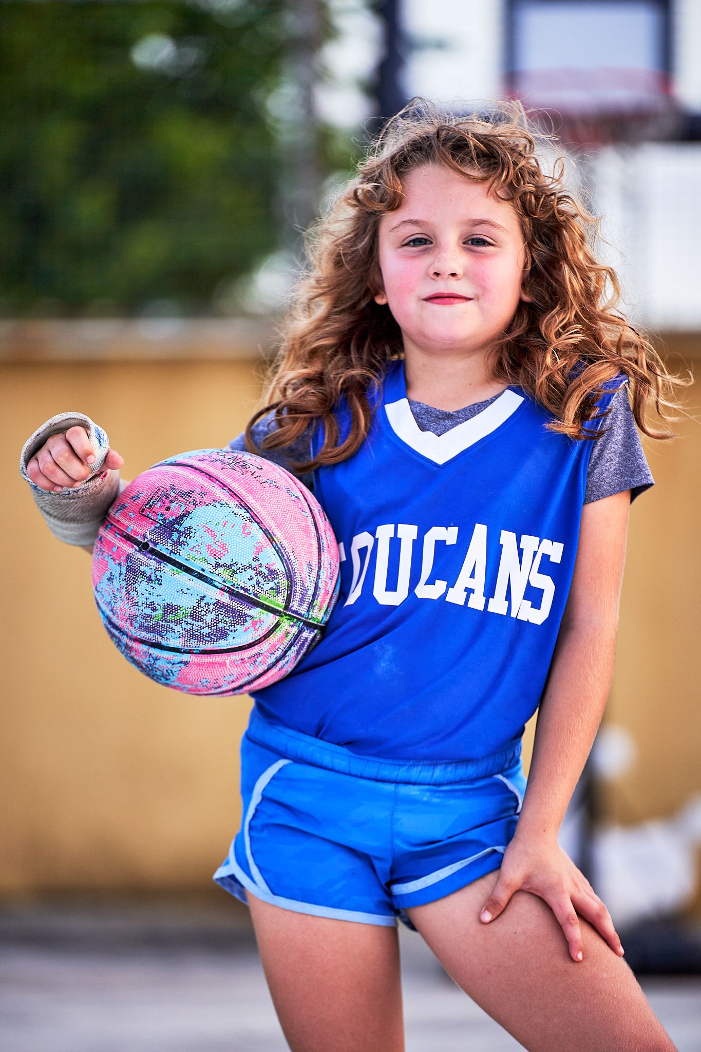 Young athlete in blue jersey holds a colorful basketball while posing playfully in multiple action shots.