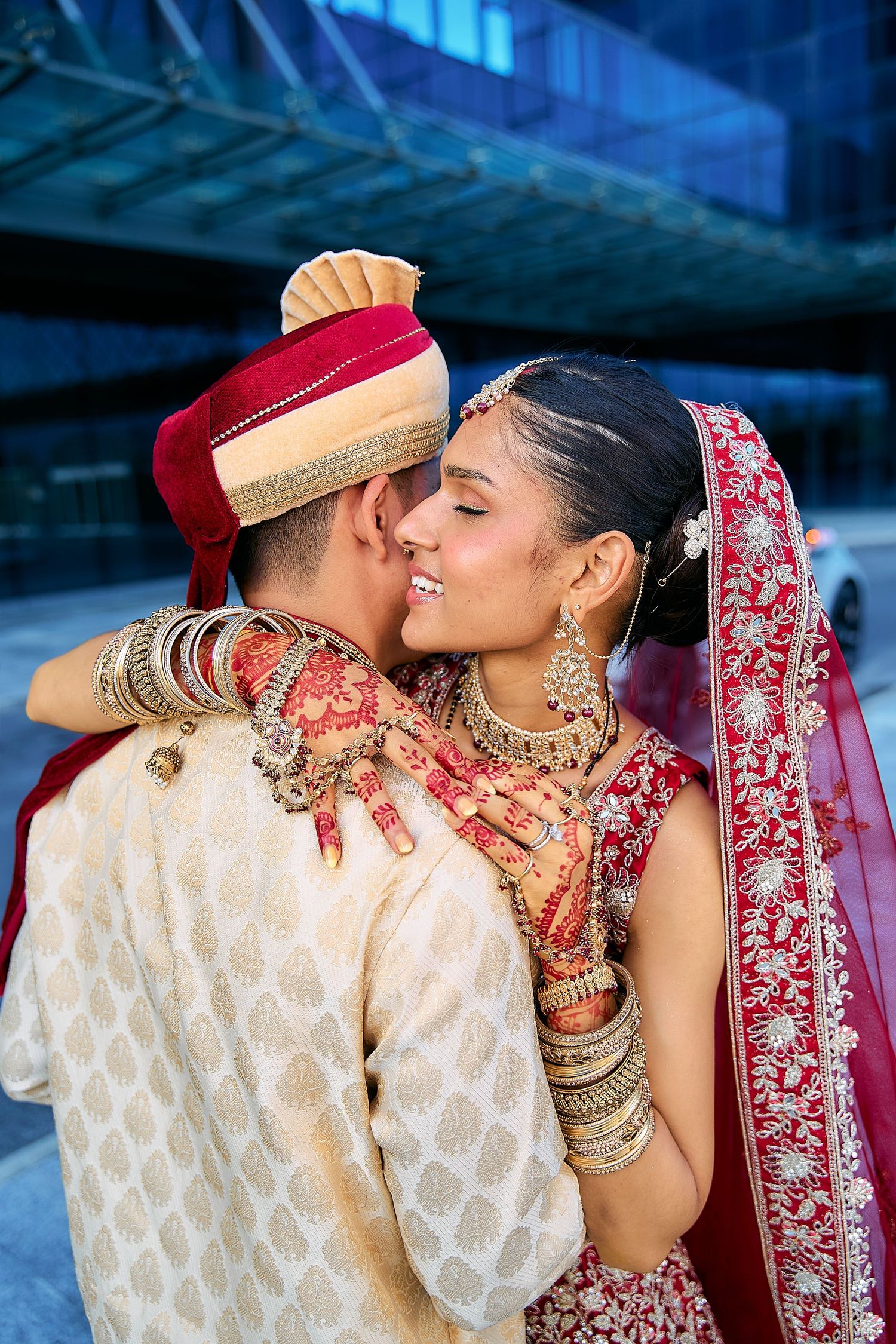Intimate wedding portraits showing couple in traditional Indian attire against glass building exterior.