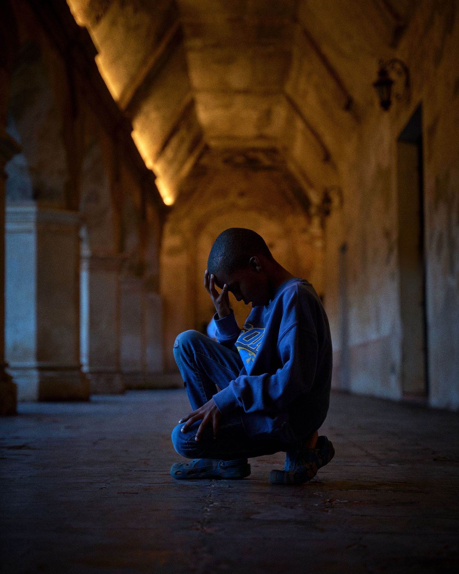 Silhouetted figure crouching in a dimly lit hallway with arched columns.
