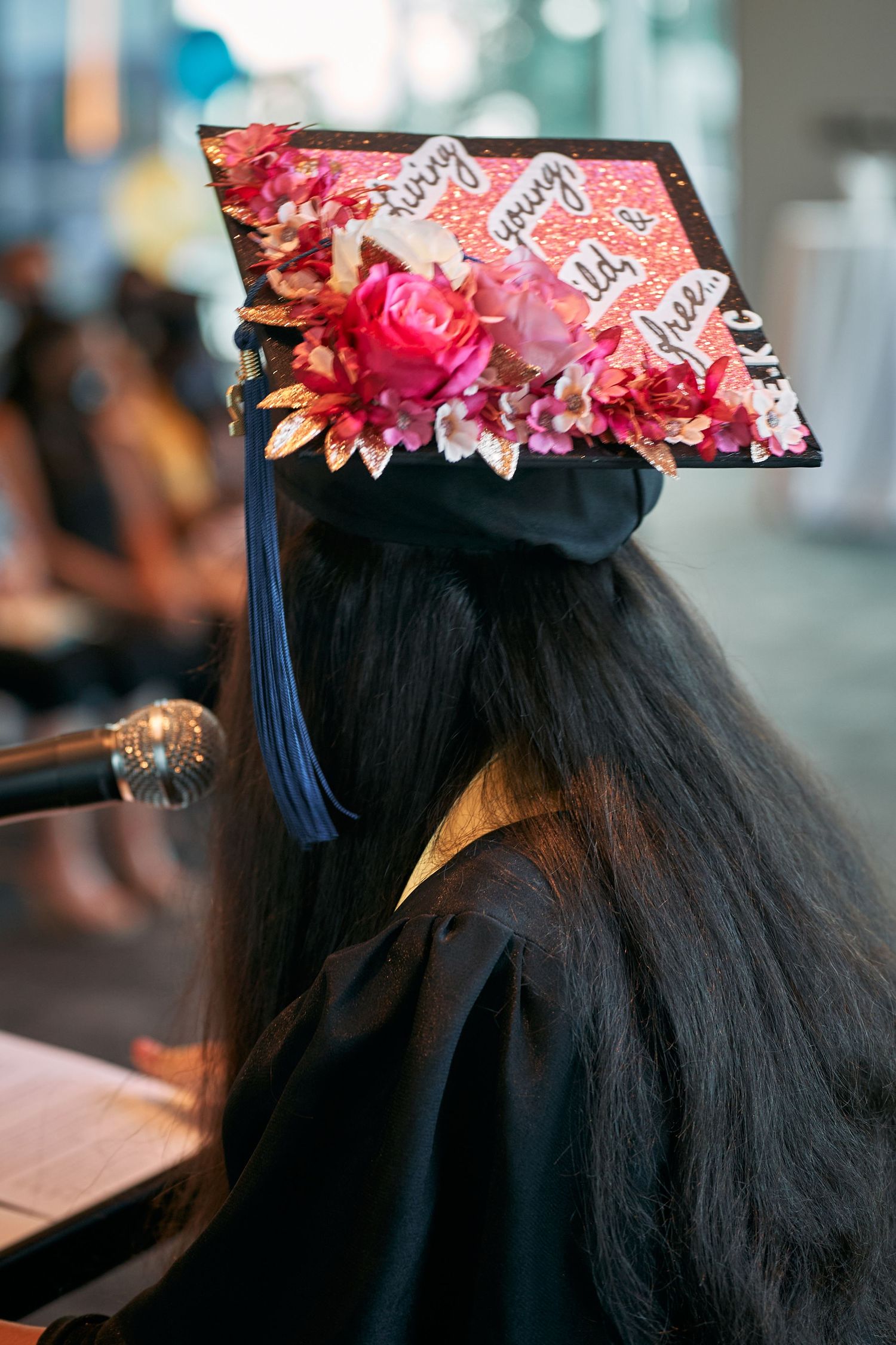 Graduation cap decorated with pink and red floral ornaments shown from multiple angles against blurred background.
