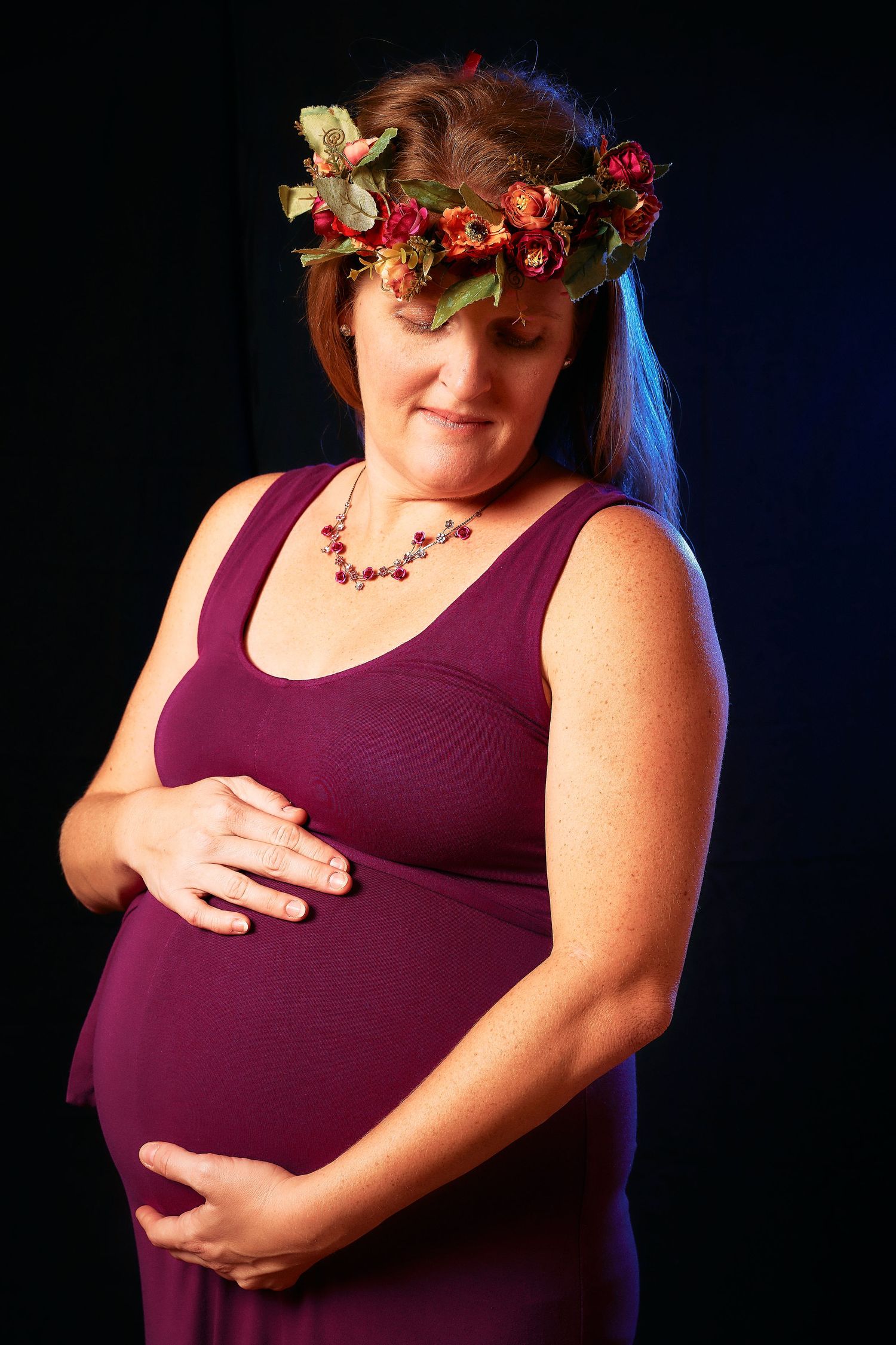 Dramatic maternity portraits with flower crown against dark background in burgundy top.