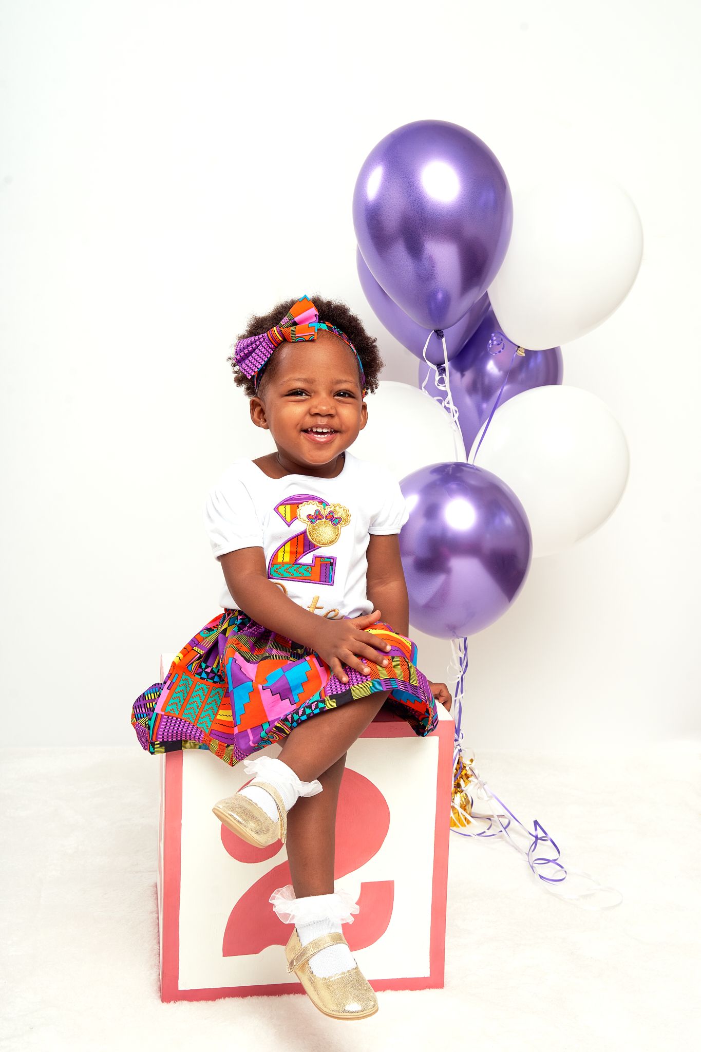 Birthday celebration photo with purple and white balloons and colorful party dress.