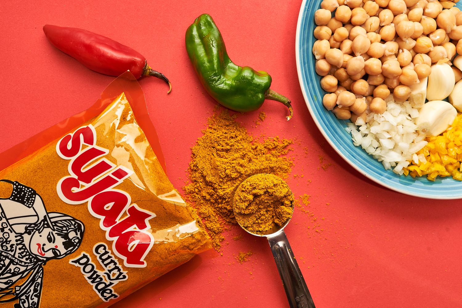 Colorful food ingredients including chickpeas, spices and peppers arranged on red background.