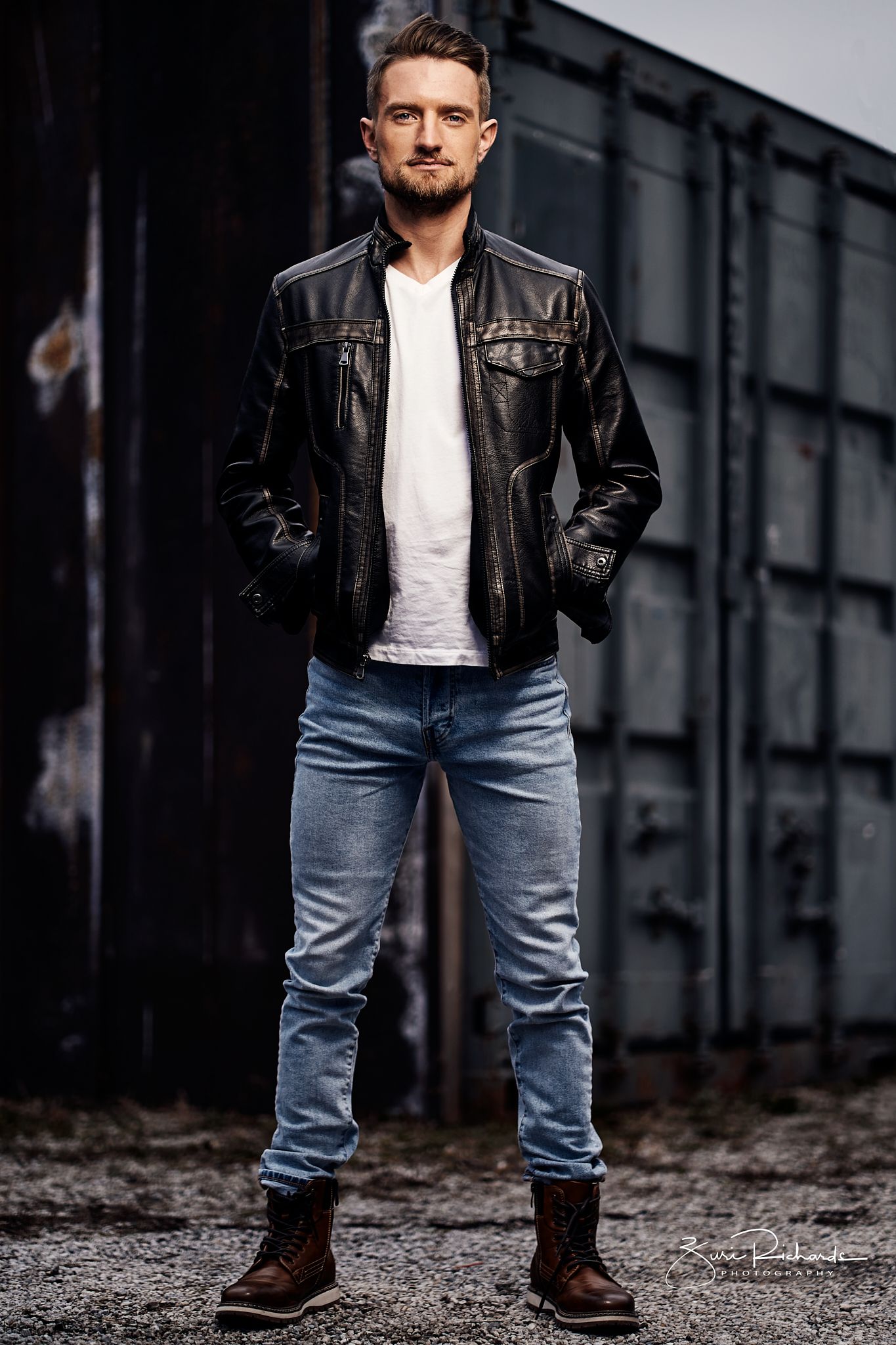 Urban fashion shoot featuring leather jacket and distressed jeans in industrial setting.