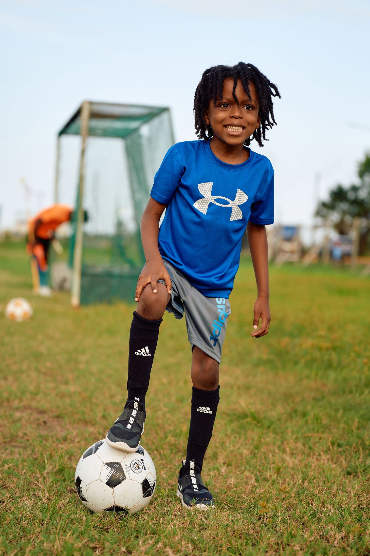 Young soccer player in blue Under Armour shirt and black socks practices dribbling skills on grassy field.