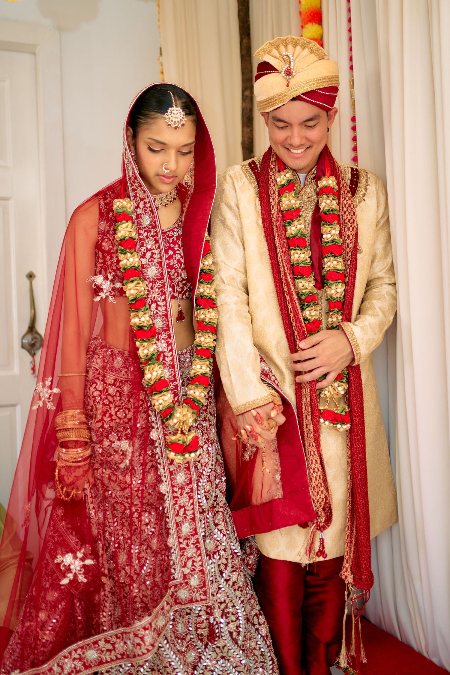Traditional Indian wedding couple in red and gold attire pose together during their ceremony celebrations.
