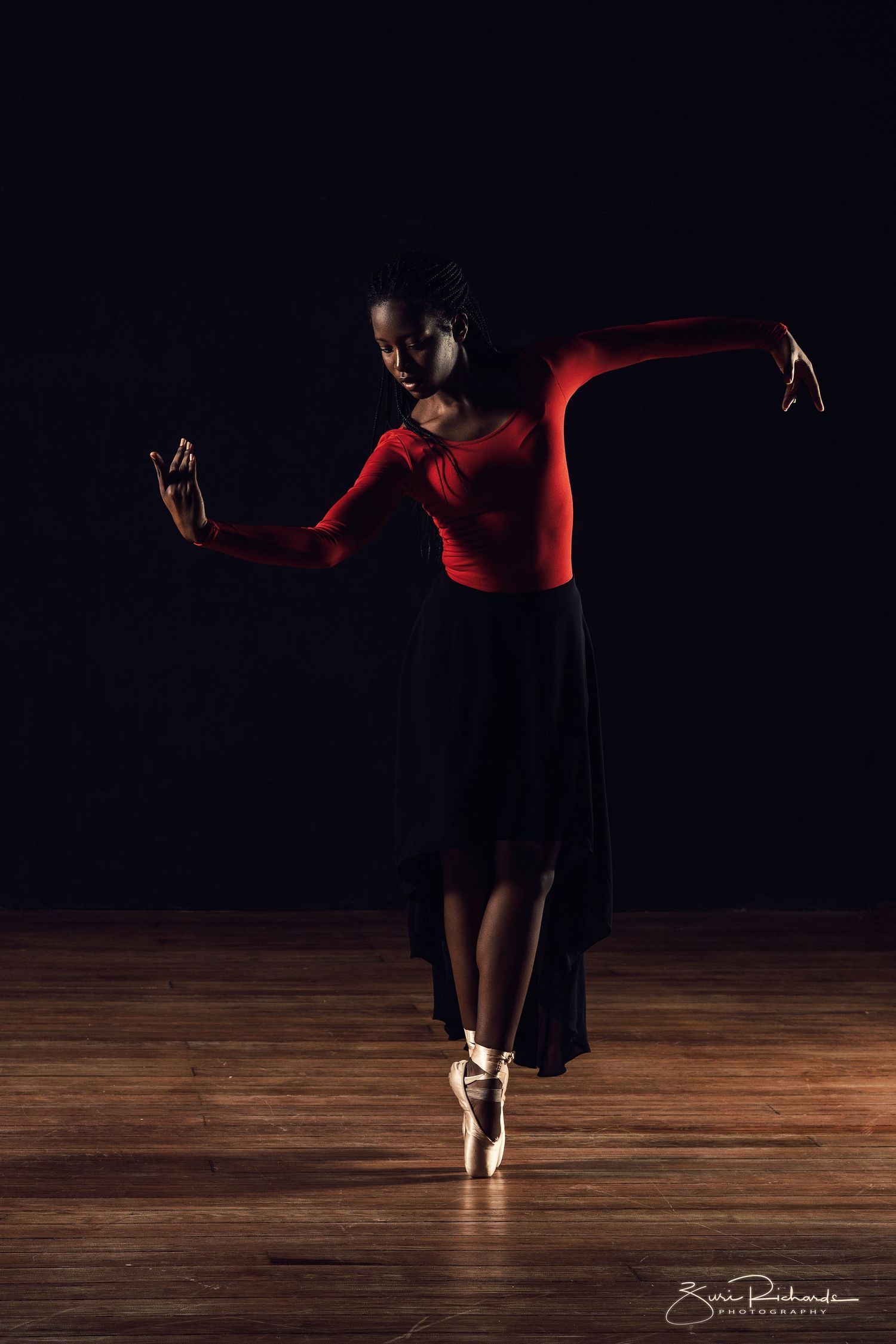 Silhouetted dancer performing graceful movements on wooden stage with dramatic lighting.