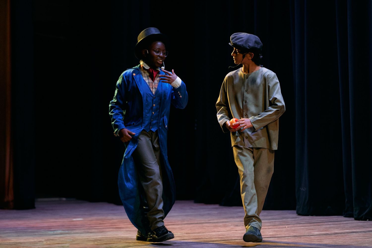 Two performers in casual workwear dance together on a dimly lit stage during a theatrical performance.