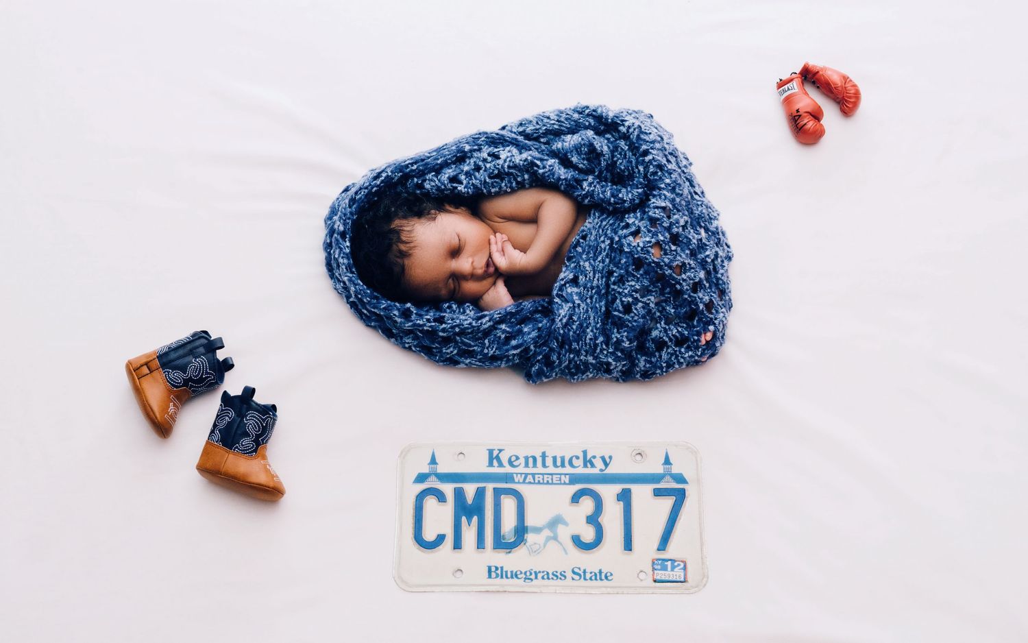 A collection of newborn photography props including a blue blanket, license plate, and wooden crate arranged on white background.