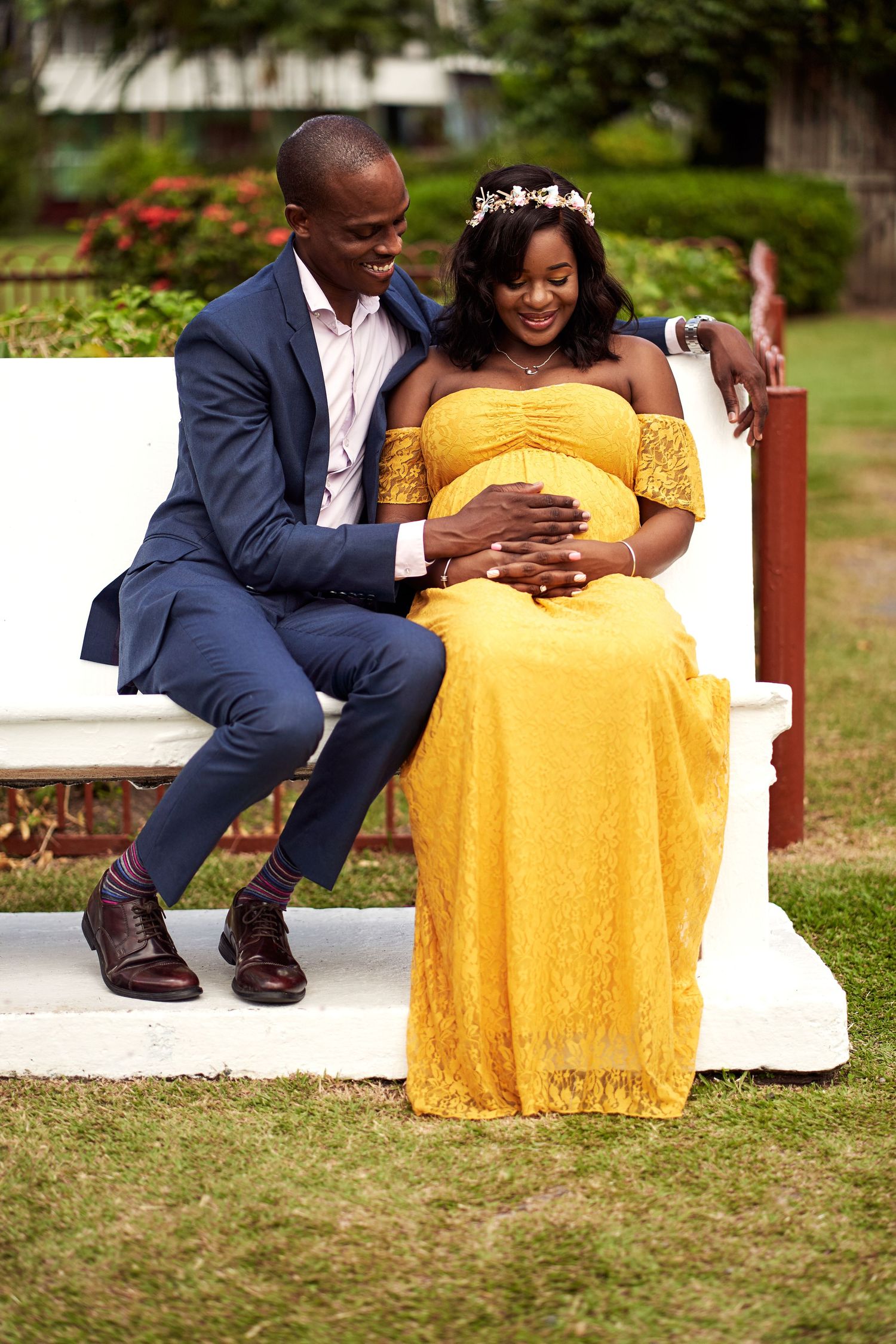 Outdoor maternity photo session featuring a couple in yellow dress and navy suit on grass.