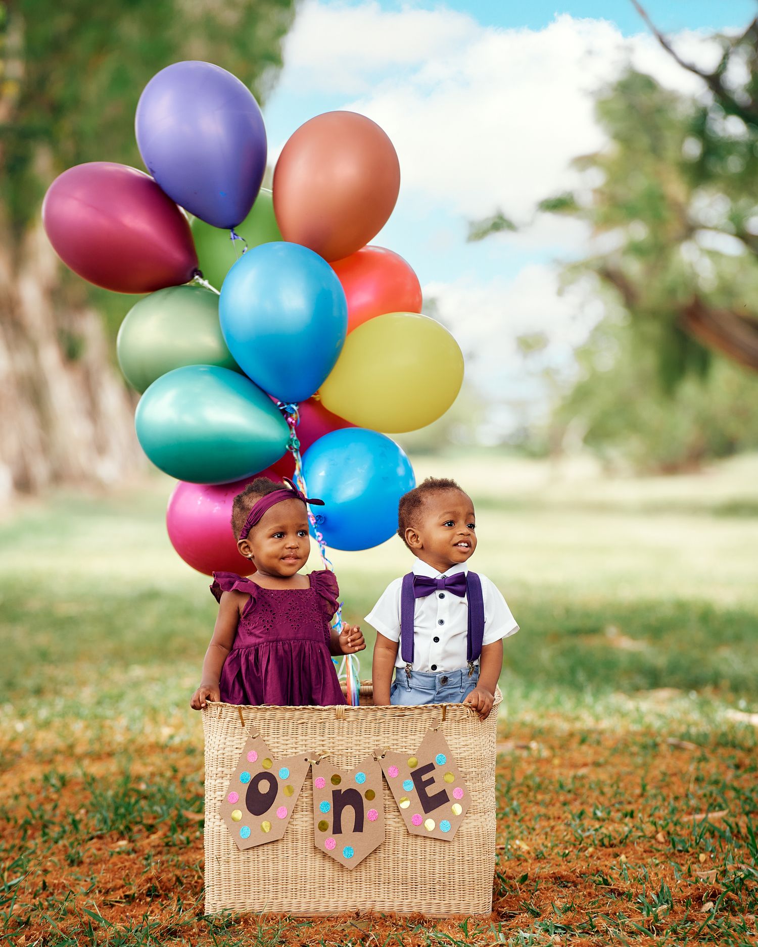 First birthday photoshoot with colorful balloons and wicker basket in a sunny field.