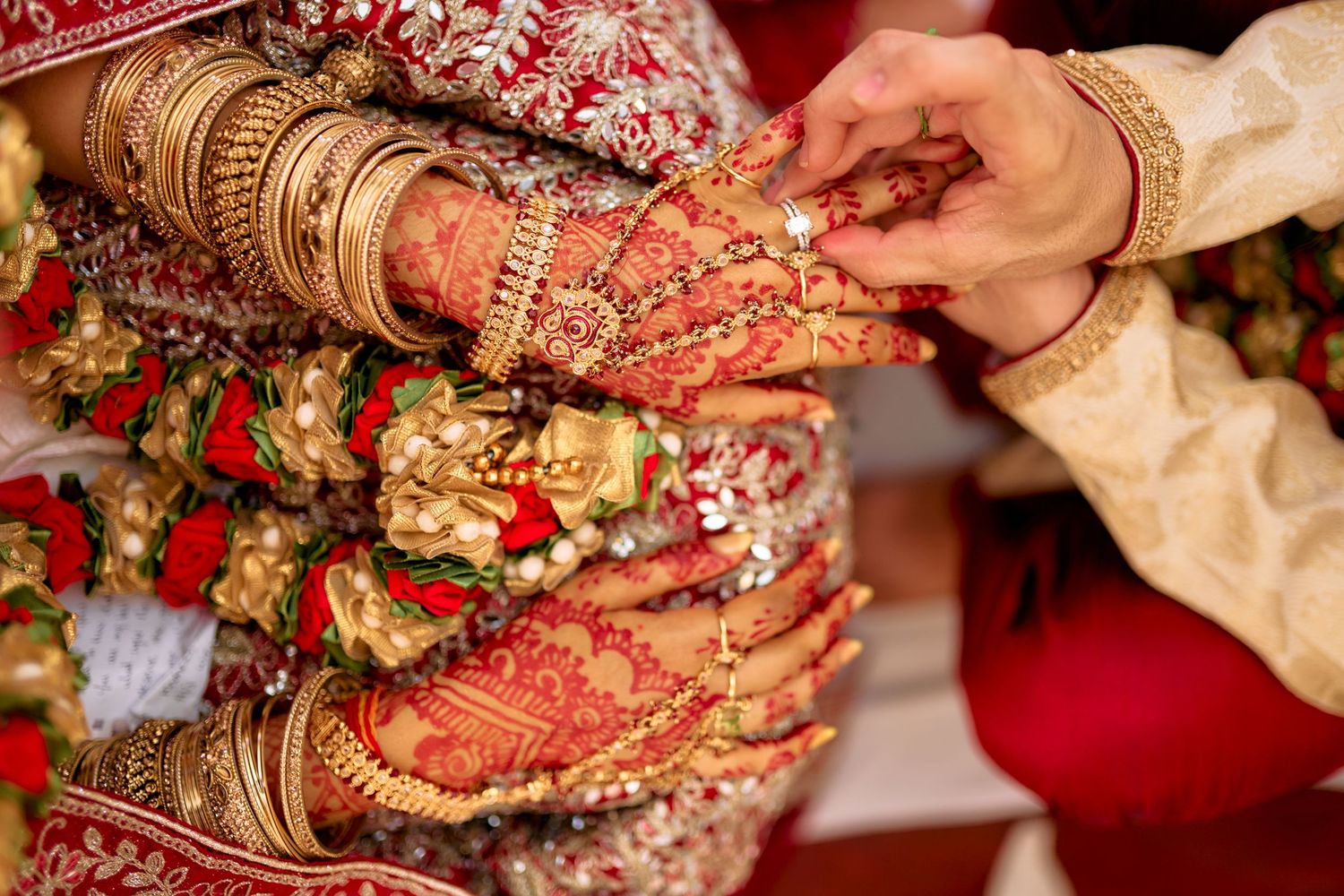 Close-up details of henna-adorned hands and wedding jewelry during traditional Indian ceremony.
