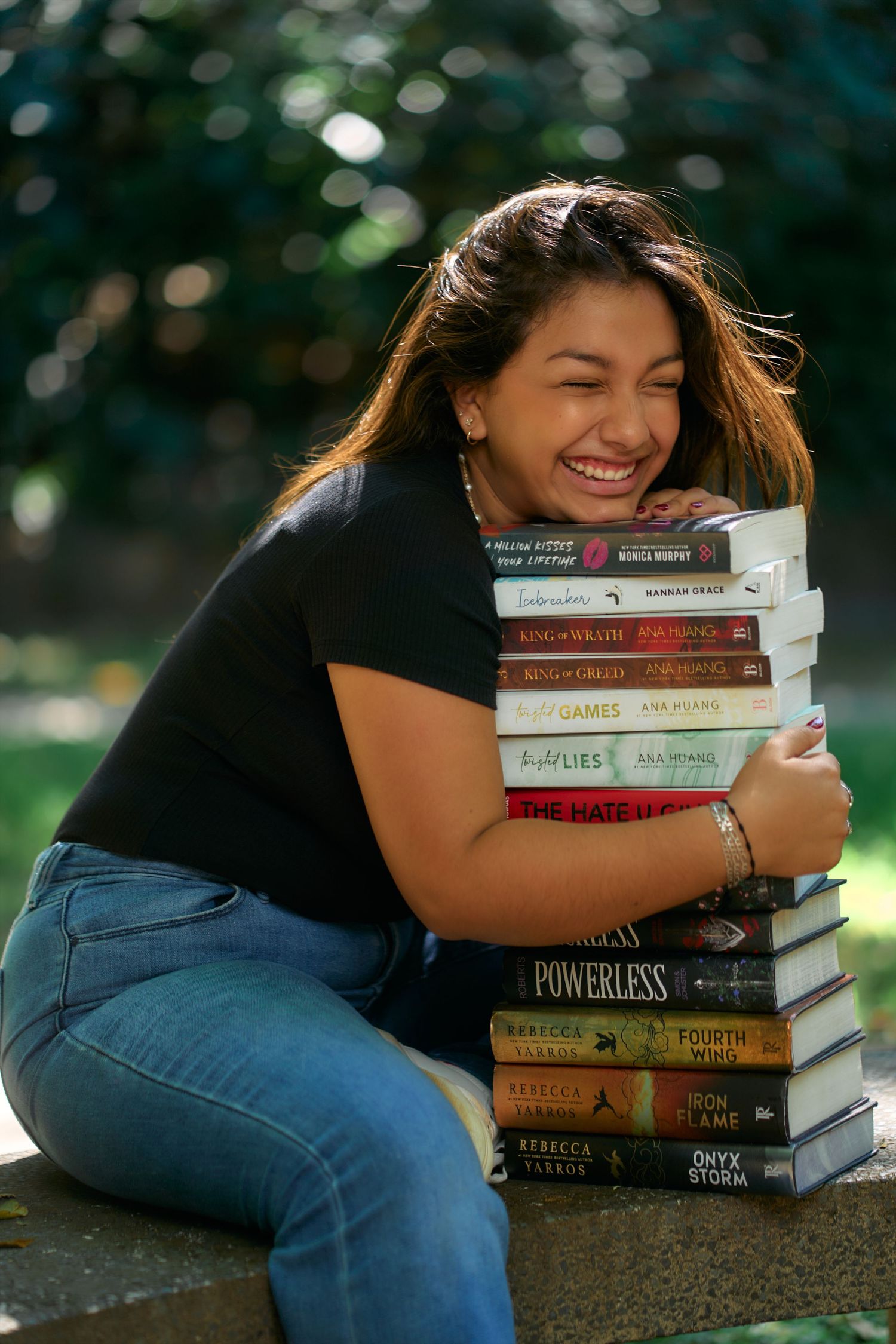 A person in jeans lying down with a stack of young adult novels and books on a textured surface outdoors.