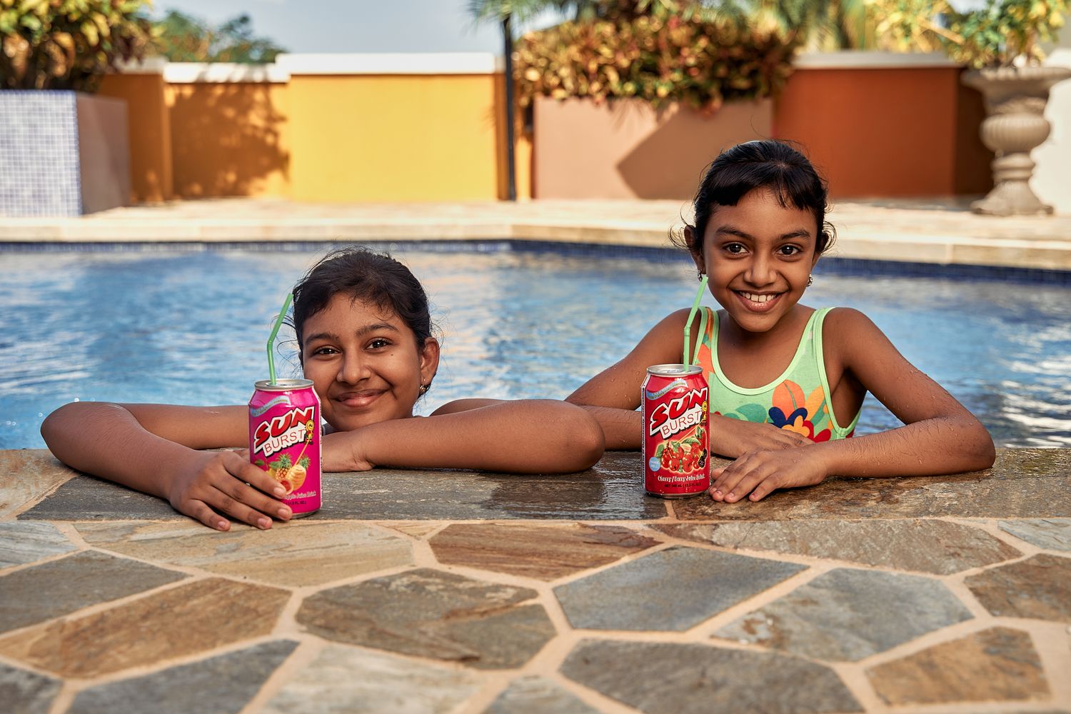 People relaxing by a pool edge with red cans of soda on a sunny day.