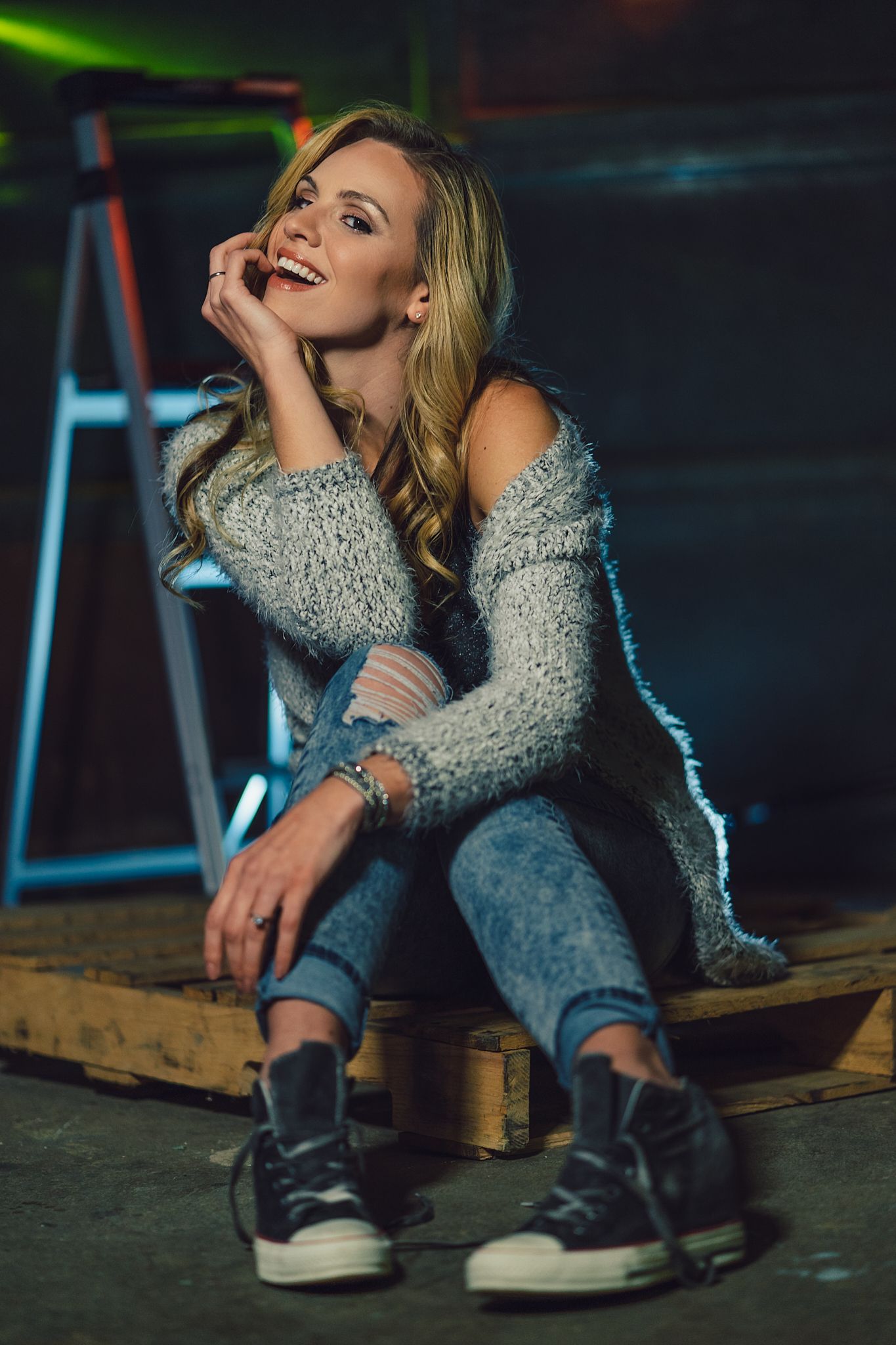 Urban fashion shoot with silver jacket and casual sneakers in dark moody lighting.