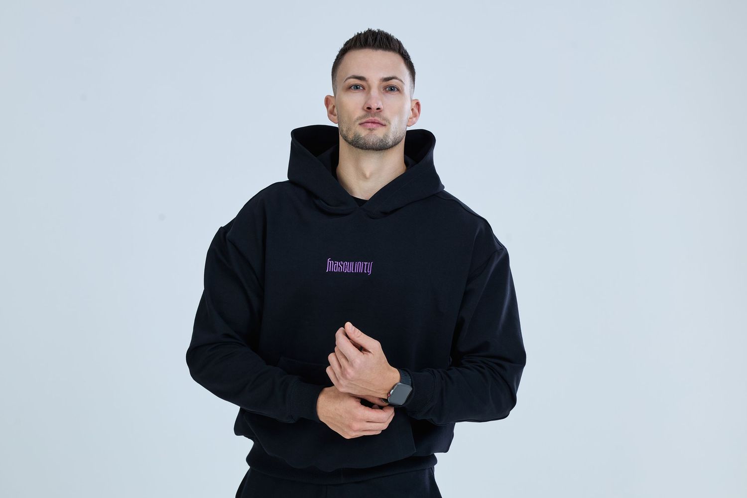 Man wearing black hoodie with purple logo, posing against light gray background.