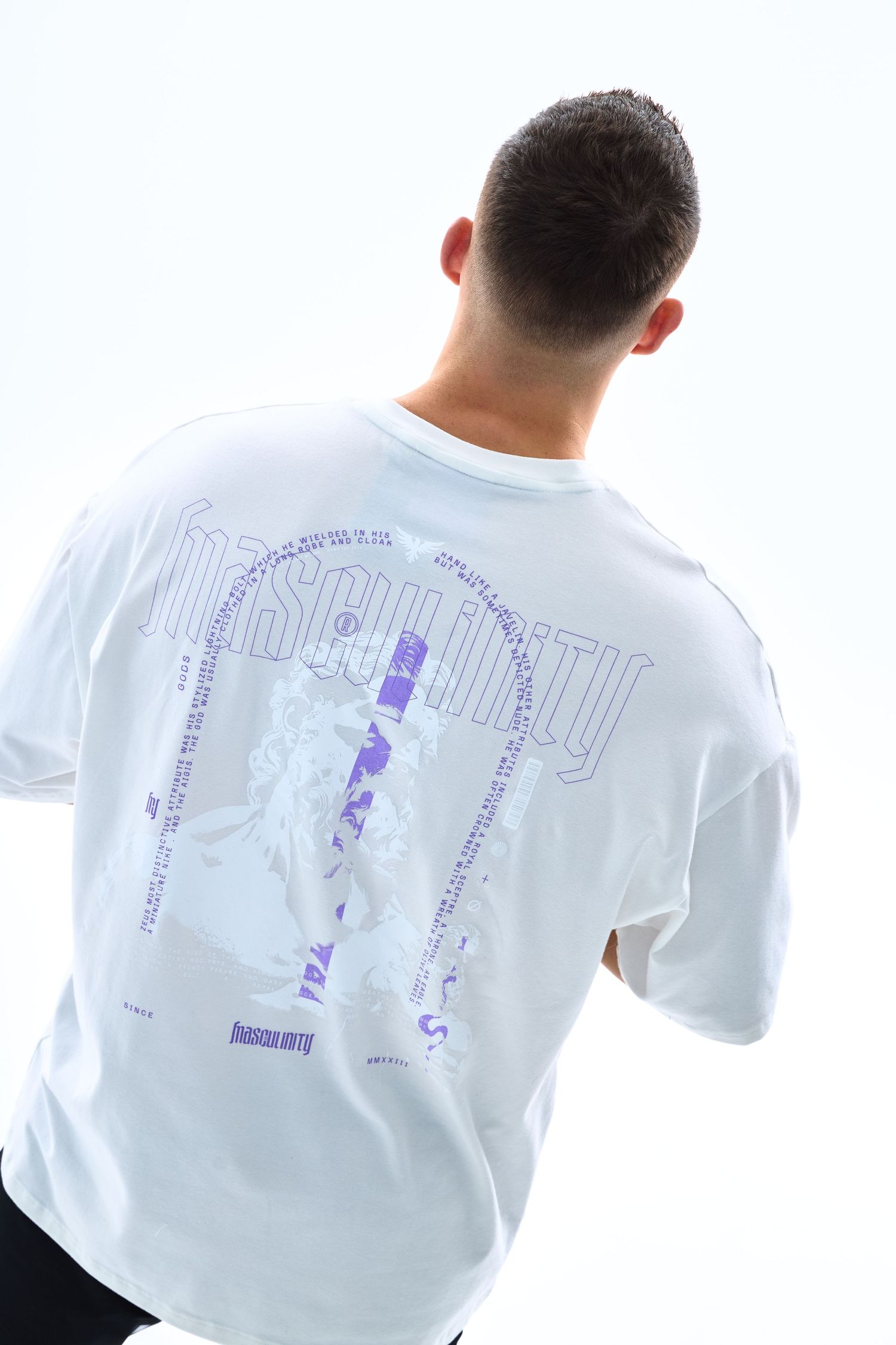 Man wearing white oversized graphic t-shirt with purple Insecurity print, photographed from behind.