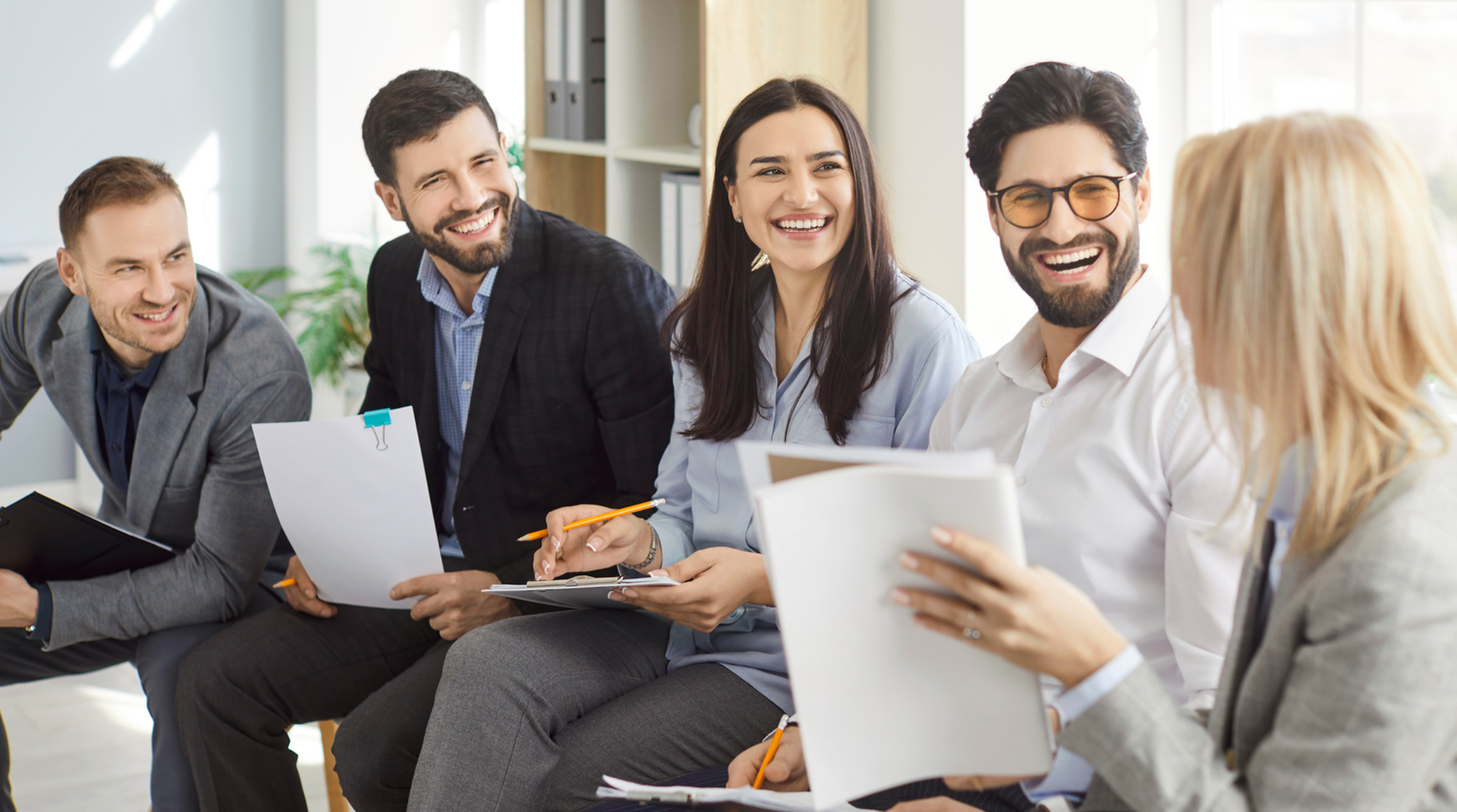 Business professionals collaborate and review documents together in a modern office meeting space.