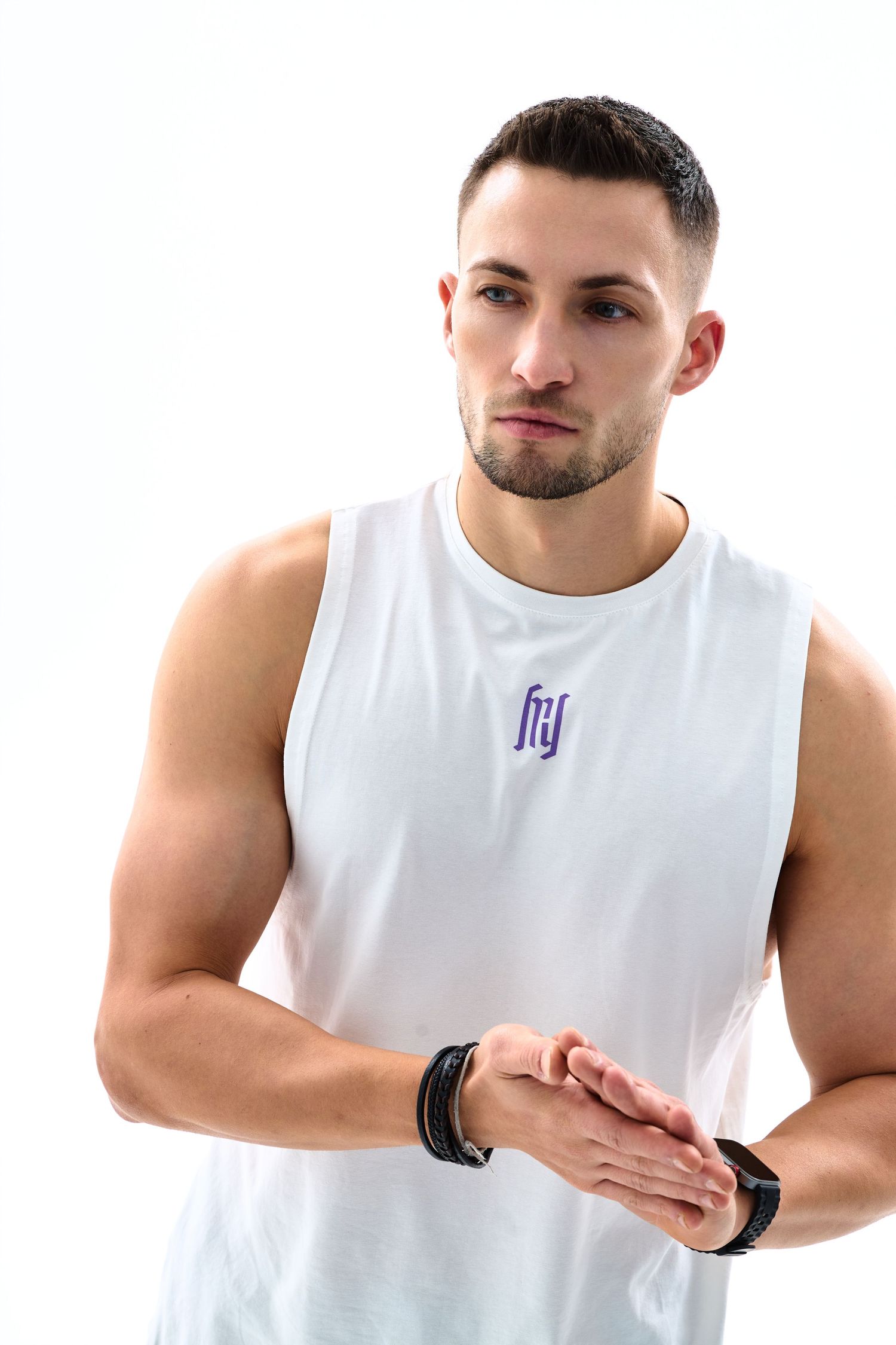Muscular man in white sleeveless FTY shirt clasping hands, wearing black wristwatch, against white background.
