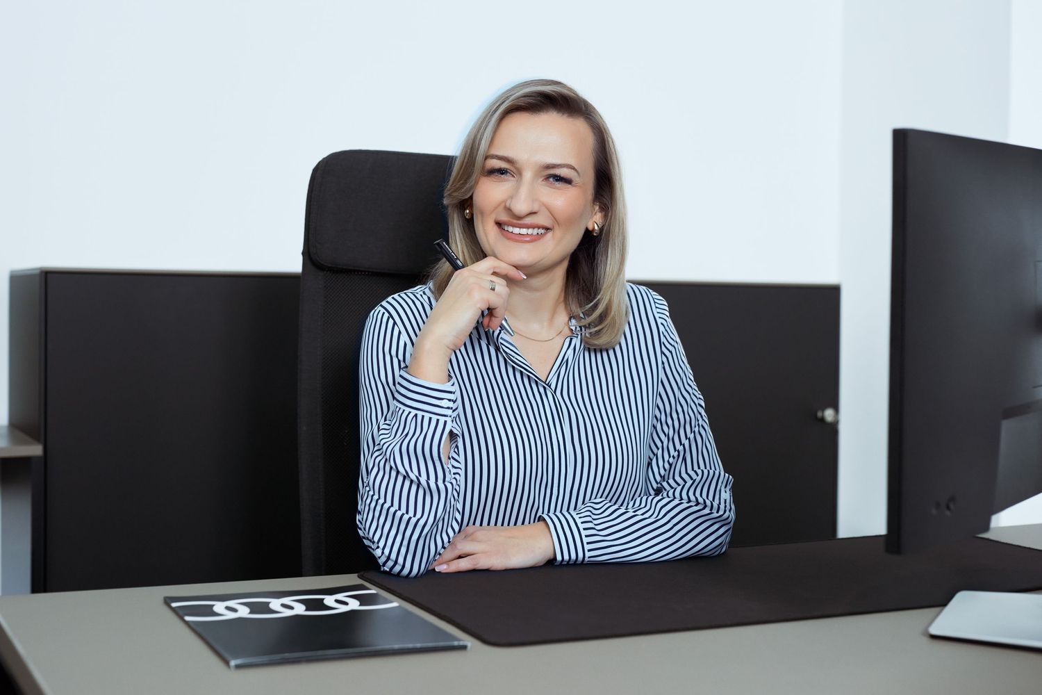 Profesjonalna kobieta w paskowanej bluzce uśmiecha się przy biurku. Fotografia biznesowa Lublin.