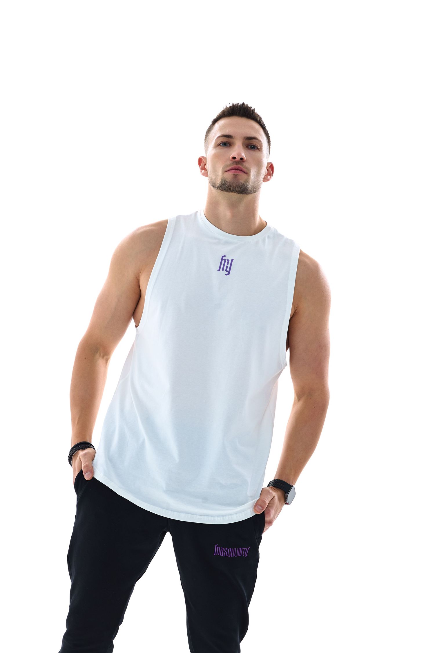Muscular man wearing a white sleeveless tank top with purple logo and black joggers on white background.