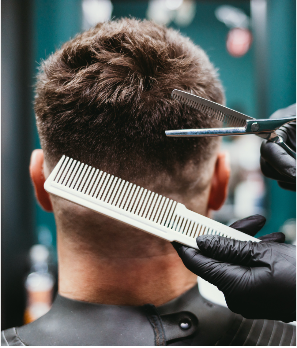 Professional barber using a white comb and clippers to create a precise haircut in a modern barbershop setting.