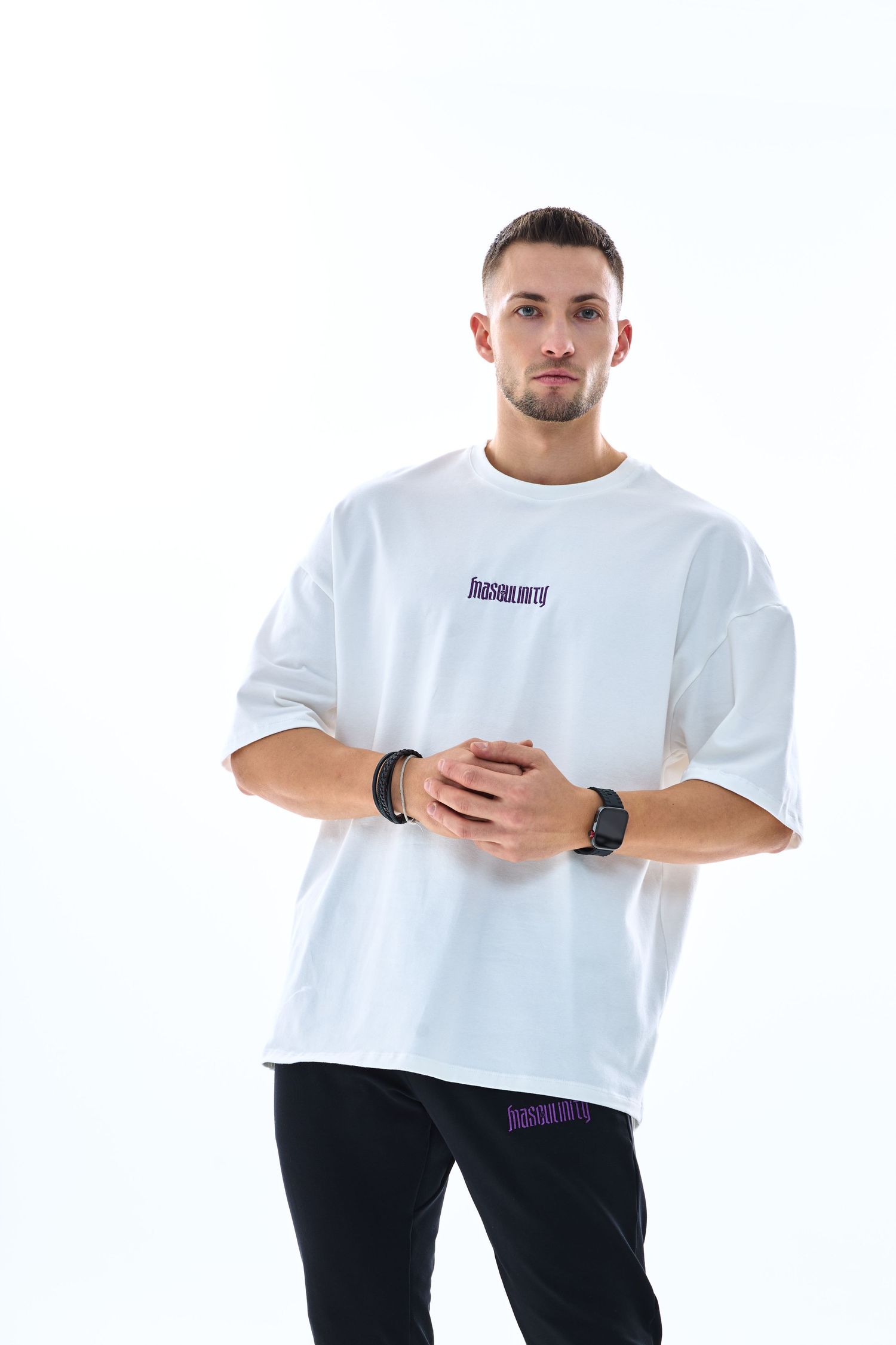 Man wearing white oversized graphic t-shirt and black pants, posing against white background.