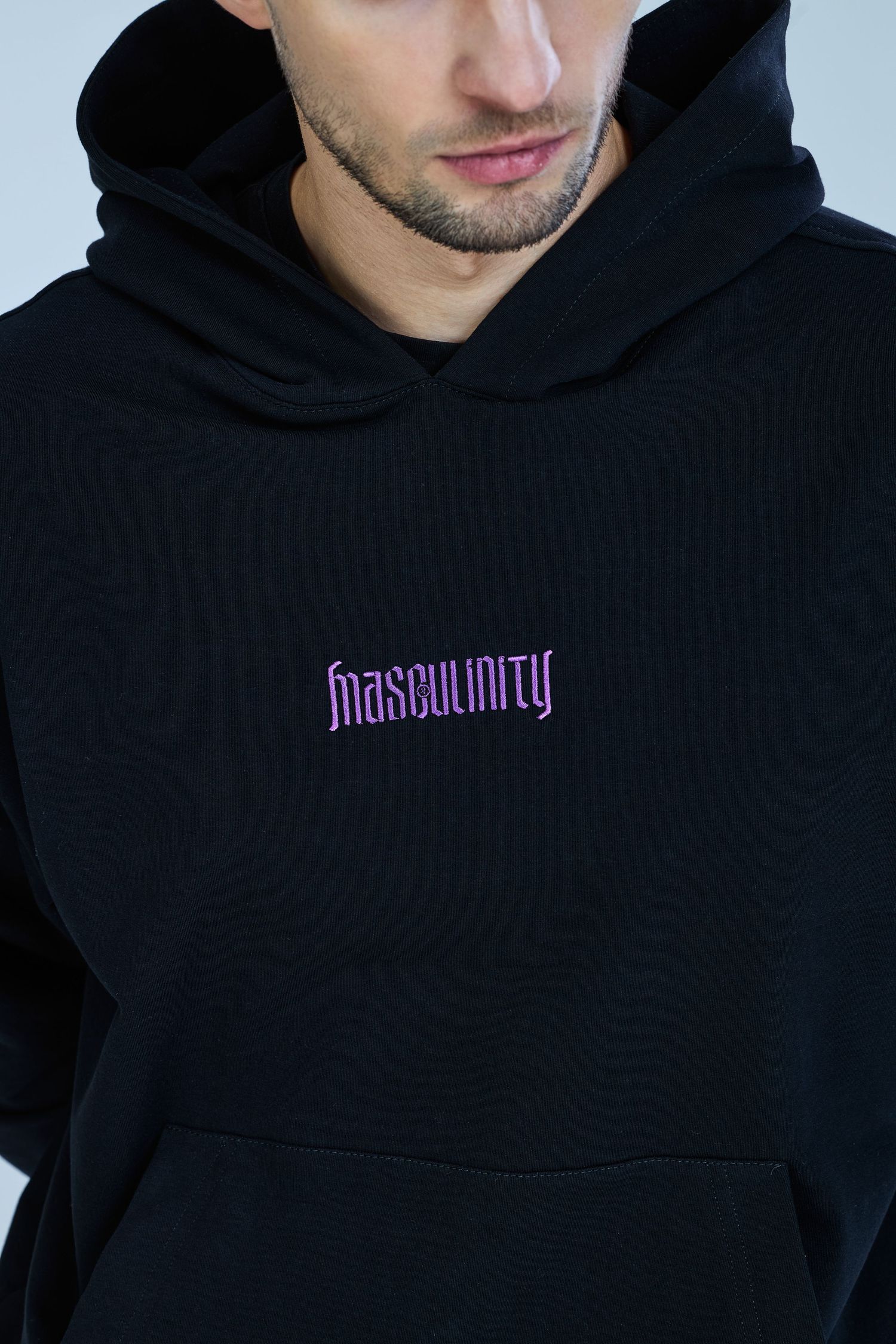 Man wearing a black hoodie with purple 'Masculinity' embroidered text on the chest.