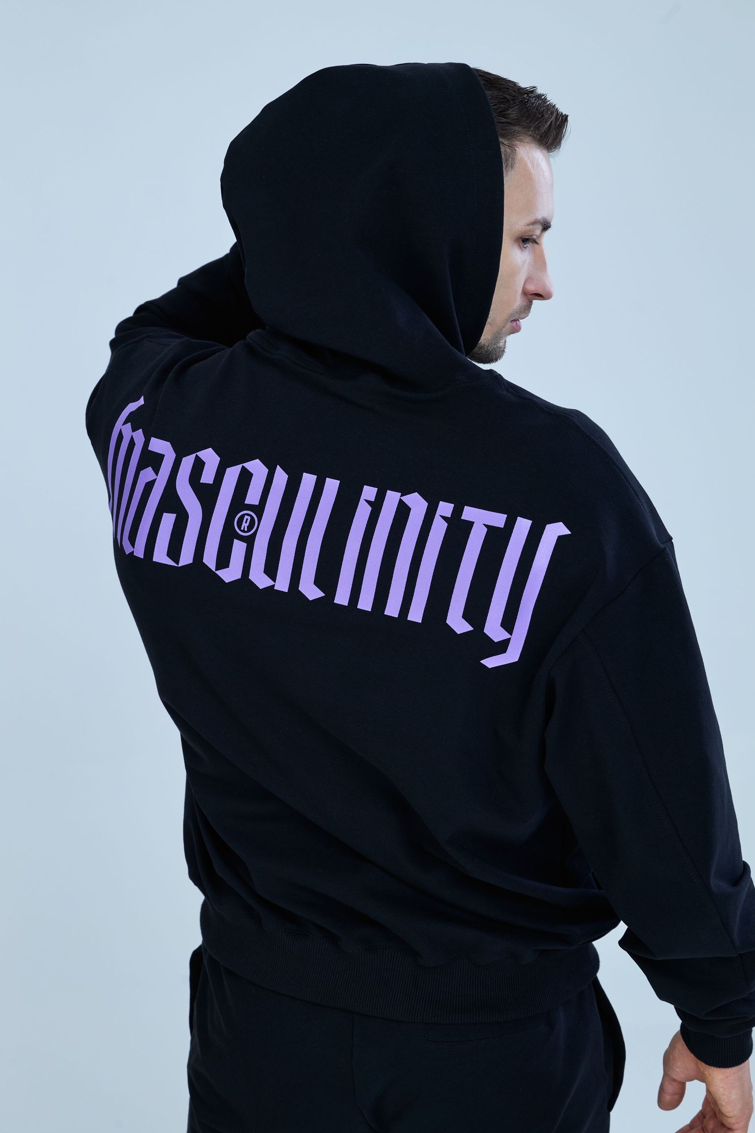 Man wearing black hoodie with purple Masculinity graphic print on back, paired with black joggers.