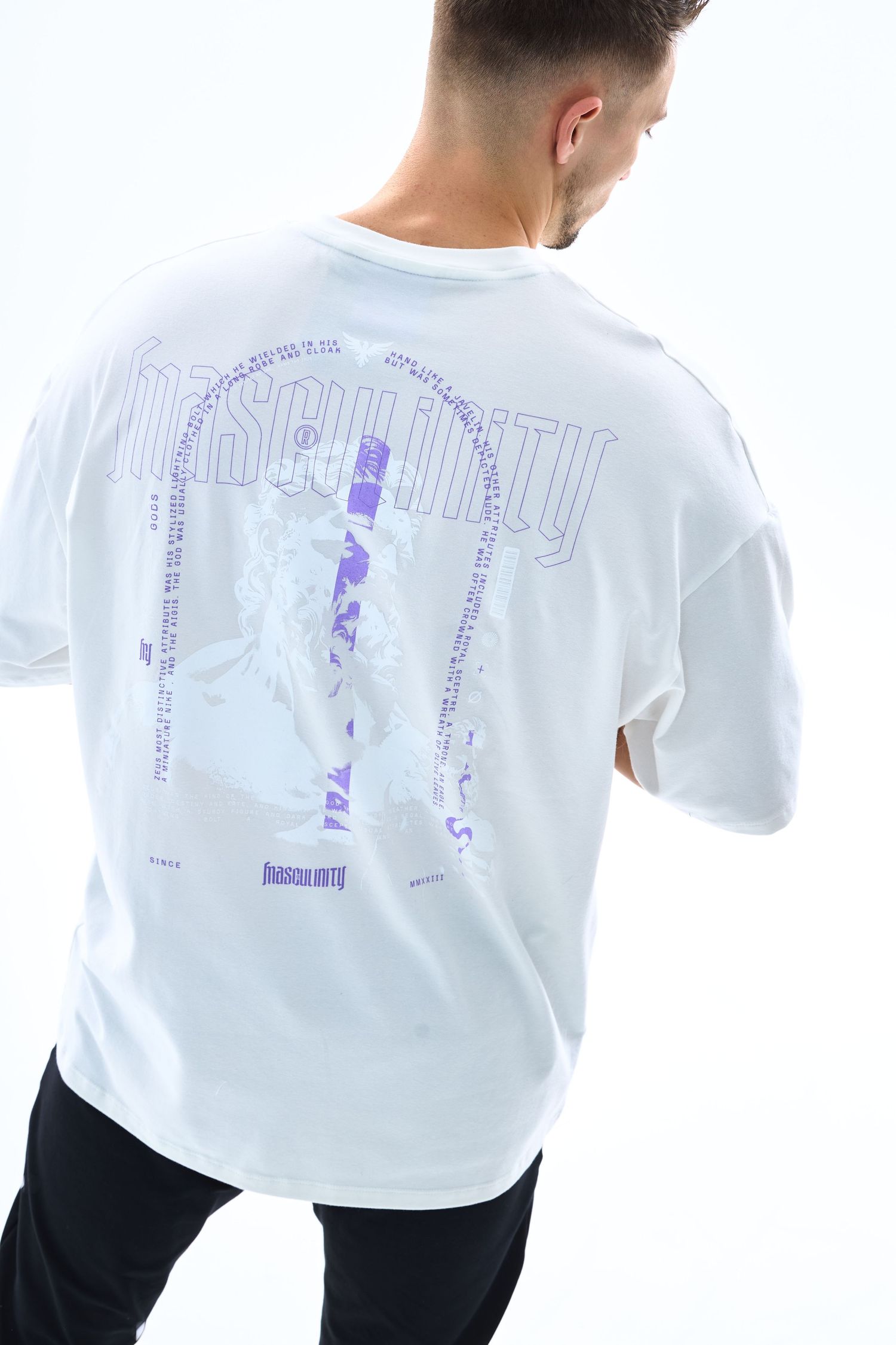 Man wearing white oversized graphic t-shirt with purple Insecurity print on back, paired with black pants.