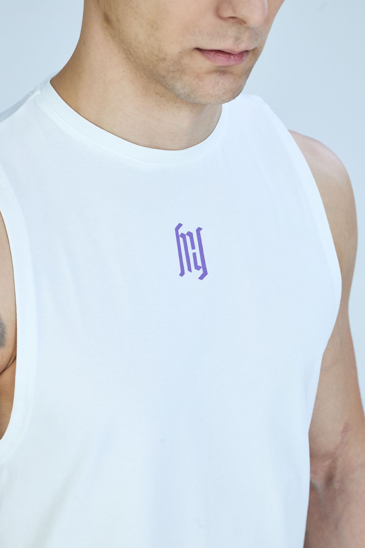 Man wearing a white sleeveless tank top with a purple logo graphic on the chest.