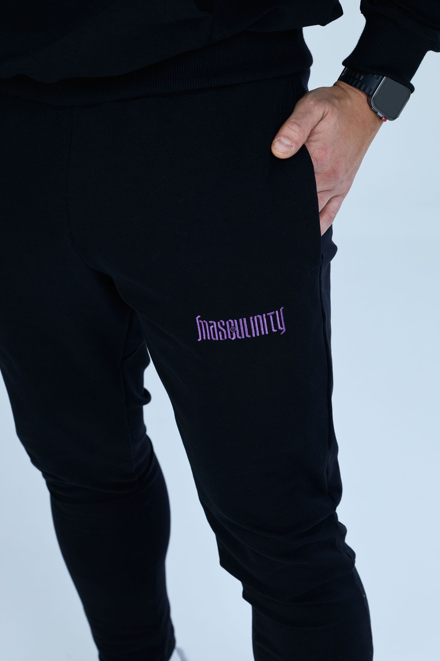 Black joggers with purple Masculinity logo embroidery, worn with a smartwatch, slim fit athletic pants.