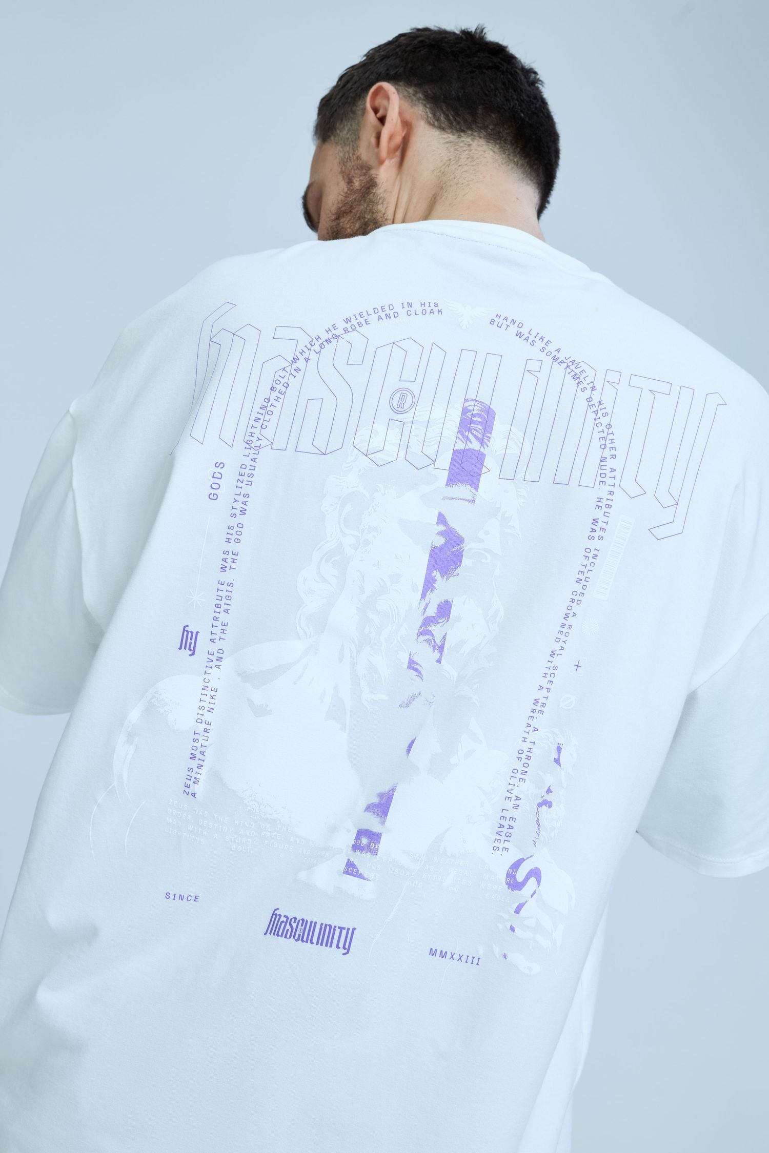White oversized t-shirt with purple Masculinity graphic print on back, worn by male model.