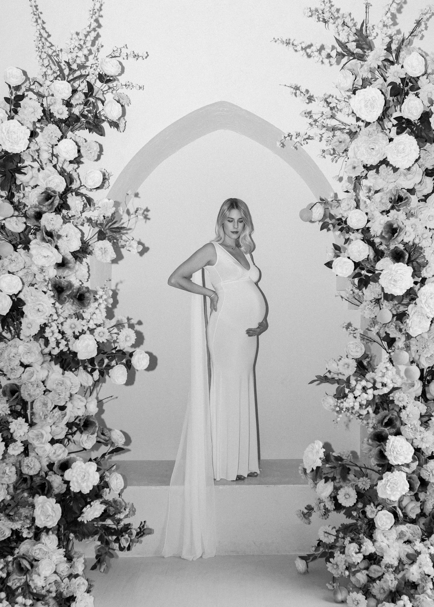 Four elegant white floral arches with cascading roses and greenery create a romantic backdrop for a wedding ceremony.