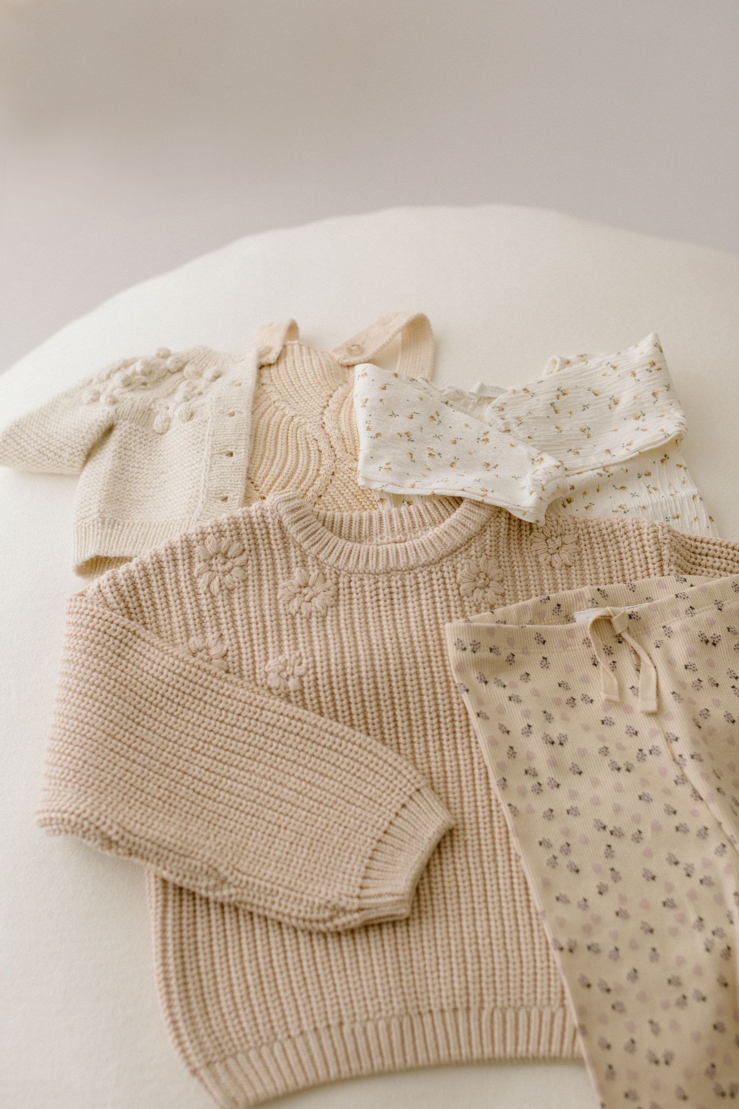 Neutral beige baby clothes with knit sweater and floral pattern pants laid flat on white surface.