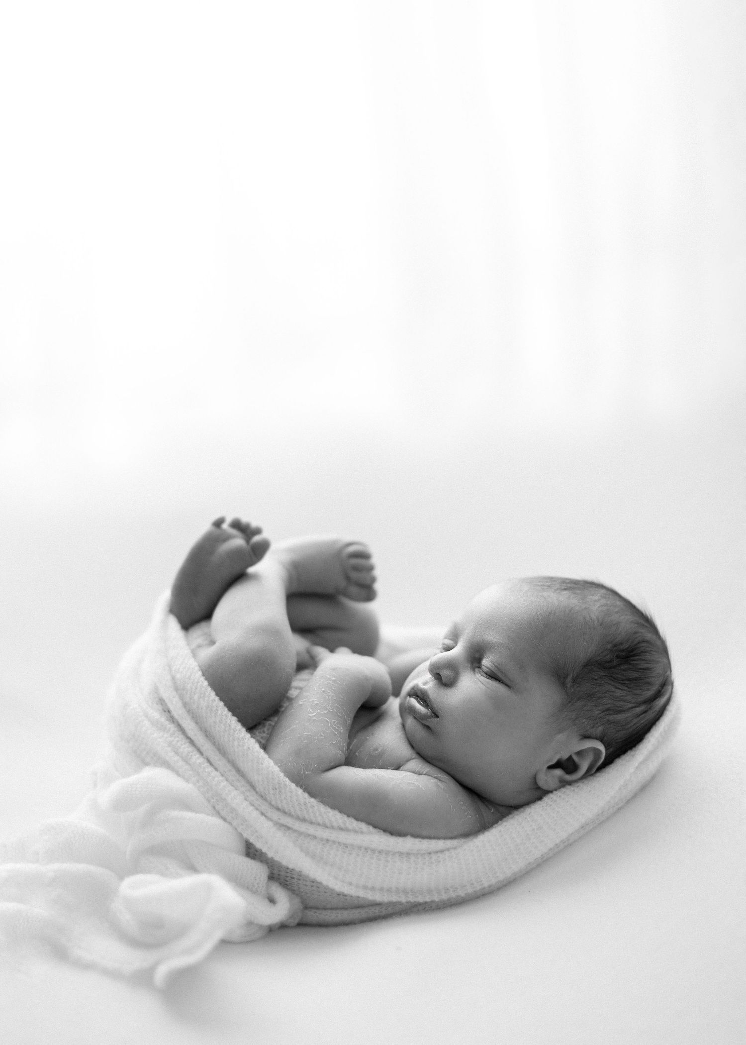 A series of black and white photos showing a sleeping newborn baby in white swaddling blankets against a light background.