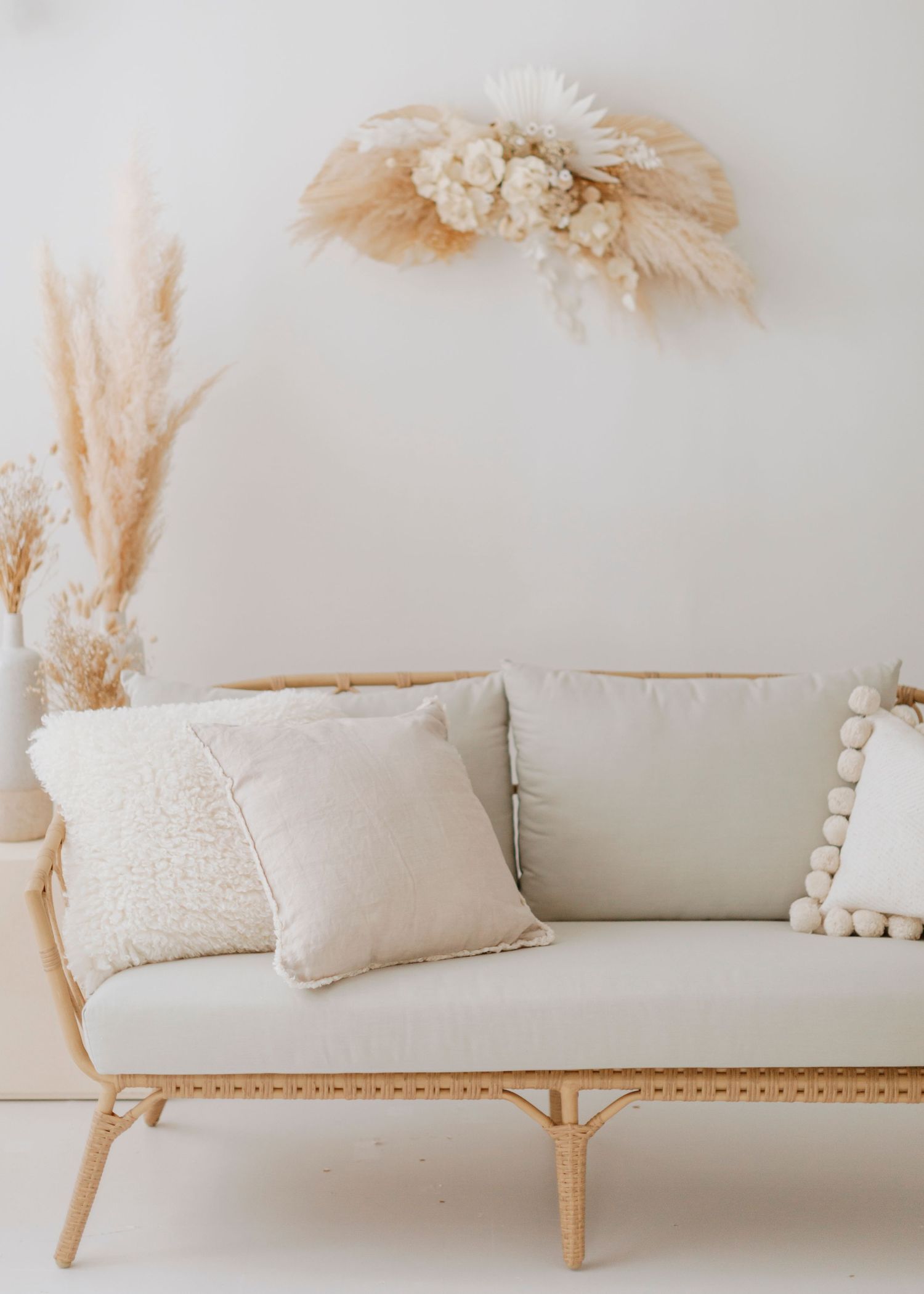 Modern boho living room decor with rattan couch, cream pillows and dried pampas grass arrangements.