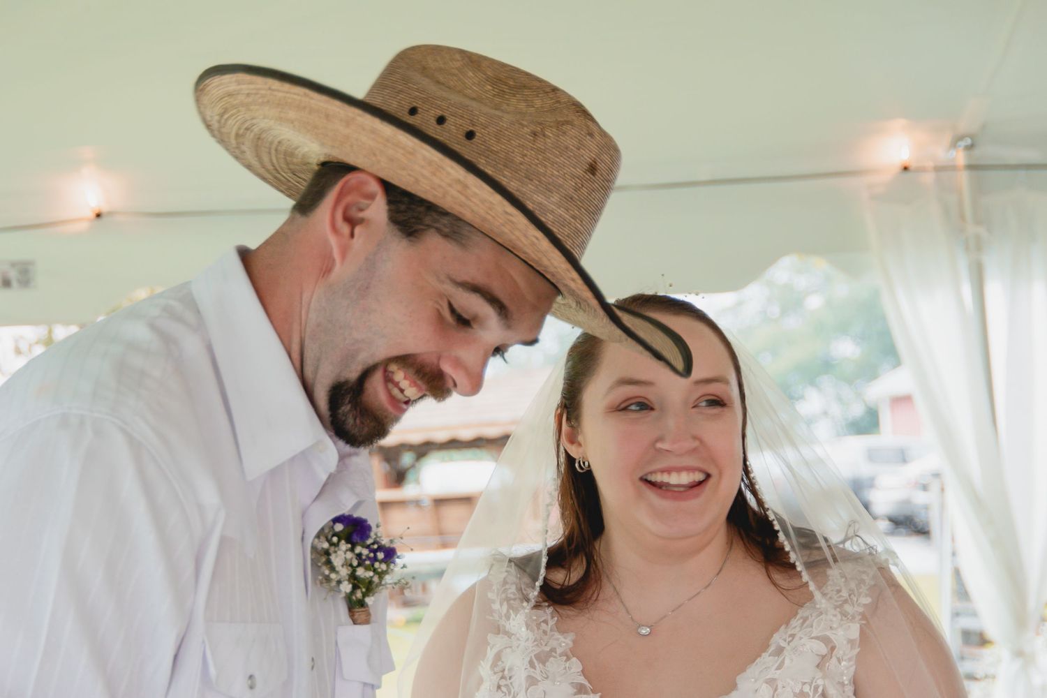 A couple in western attire shares a romantic moment during their outdoor wedding celebration.