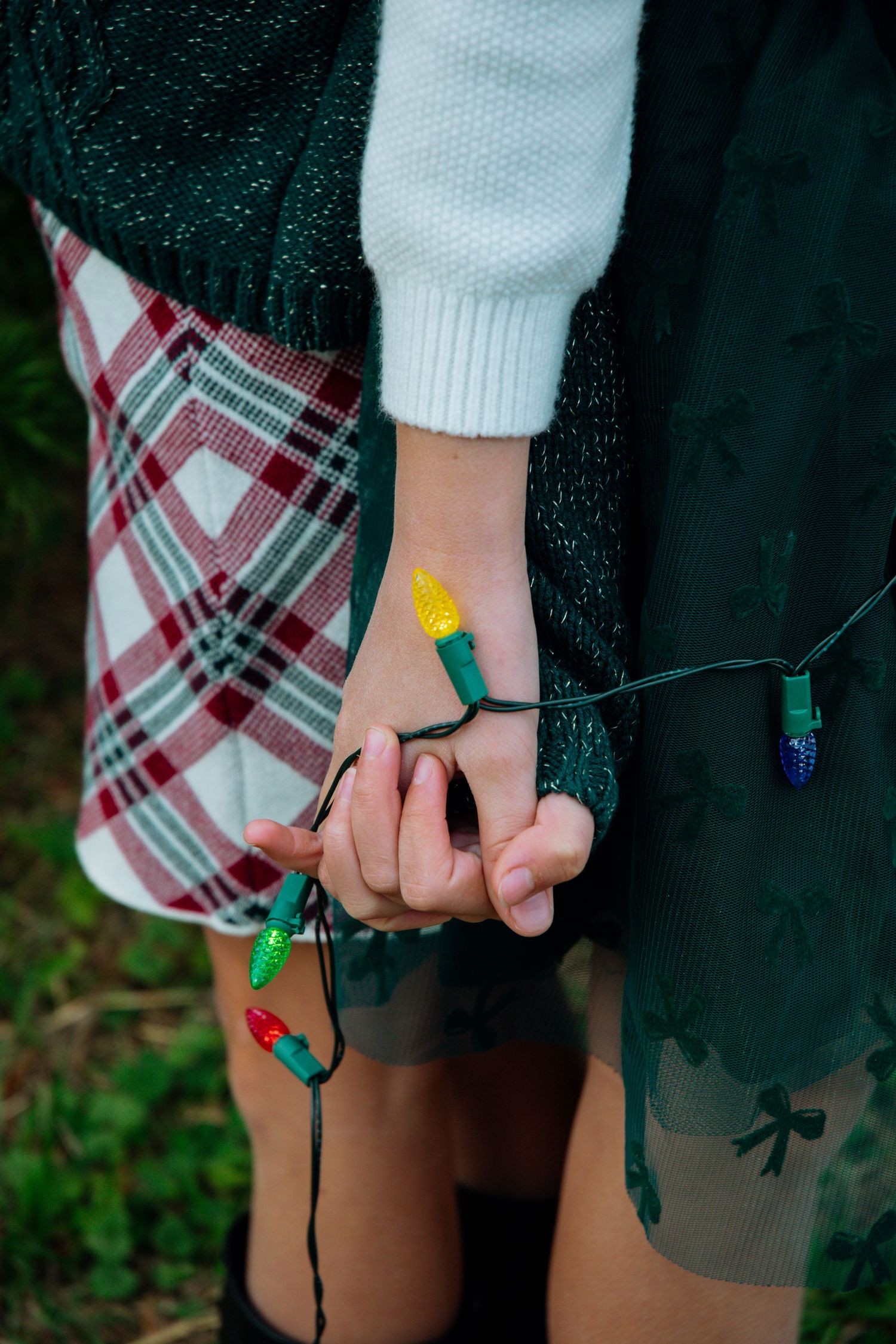 Close-up of hands holding colorful Christmas lights against dark clothing.