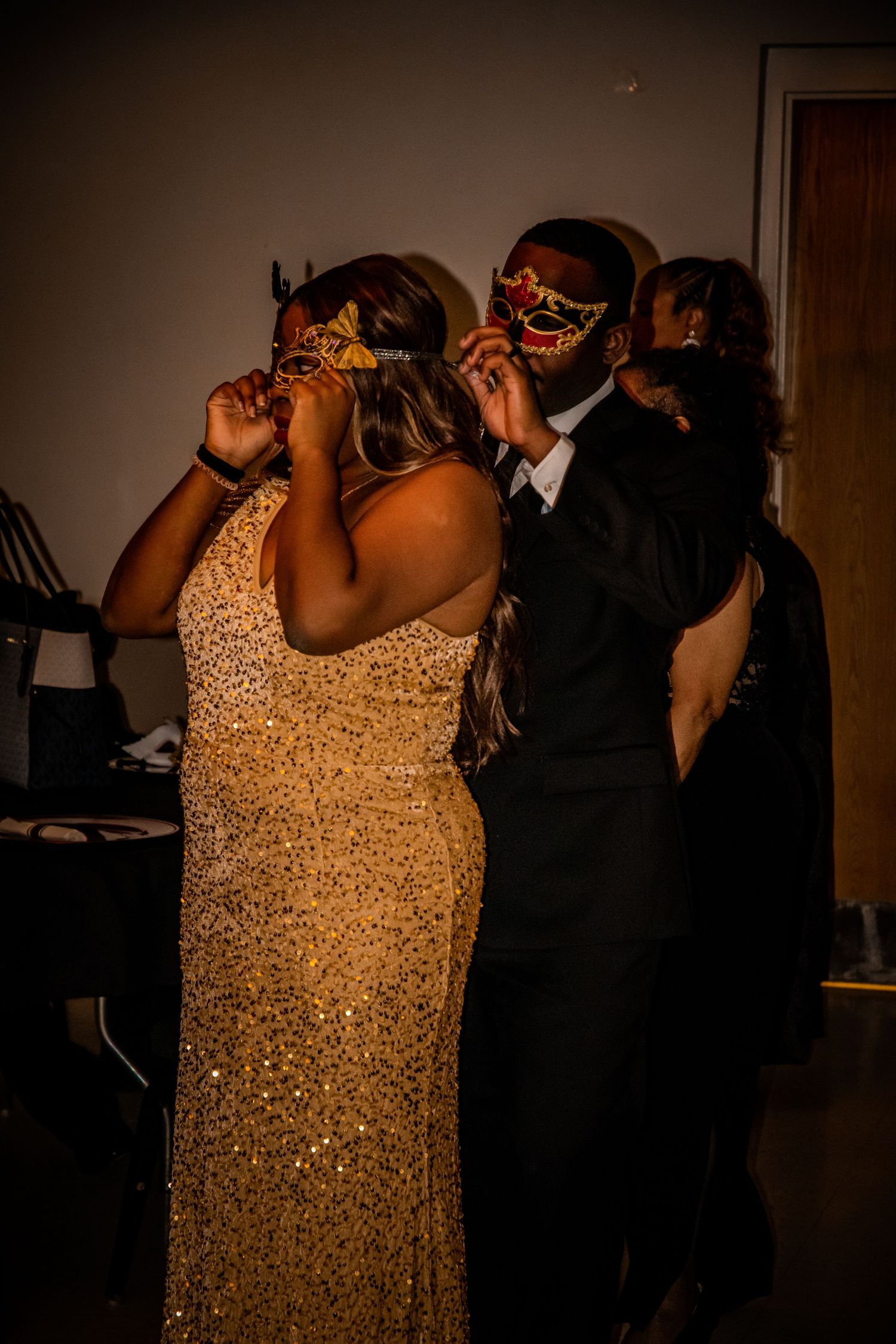 Dancers in sparkling gold dresses and dark formal wear move across a dimly lit dance floor.
